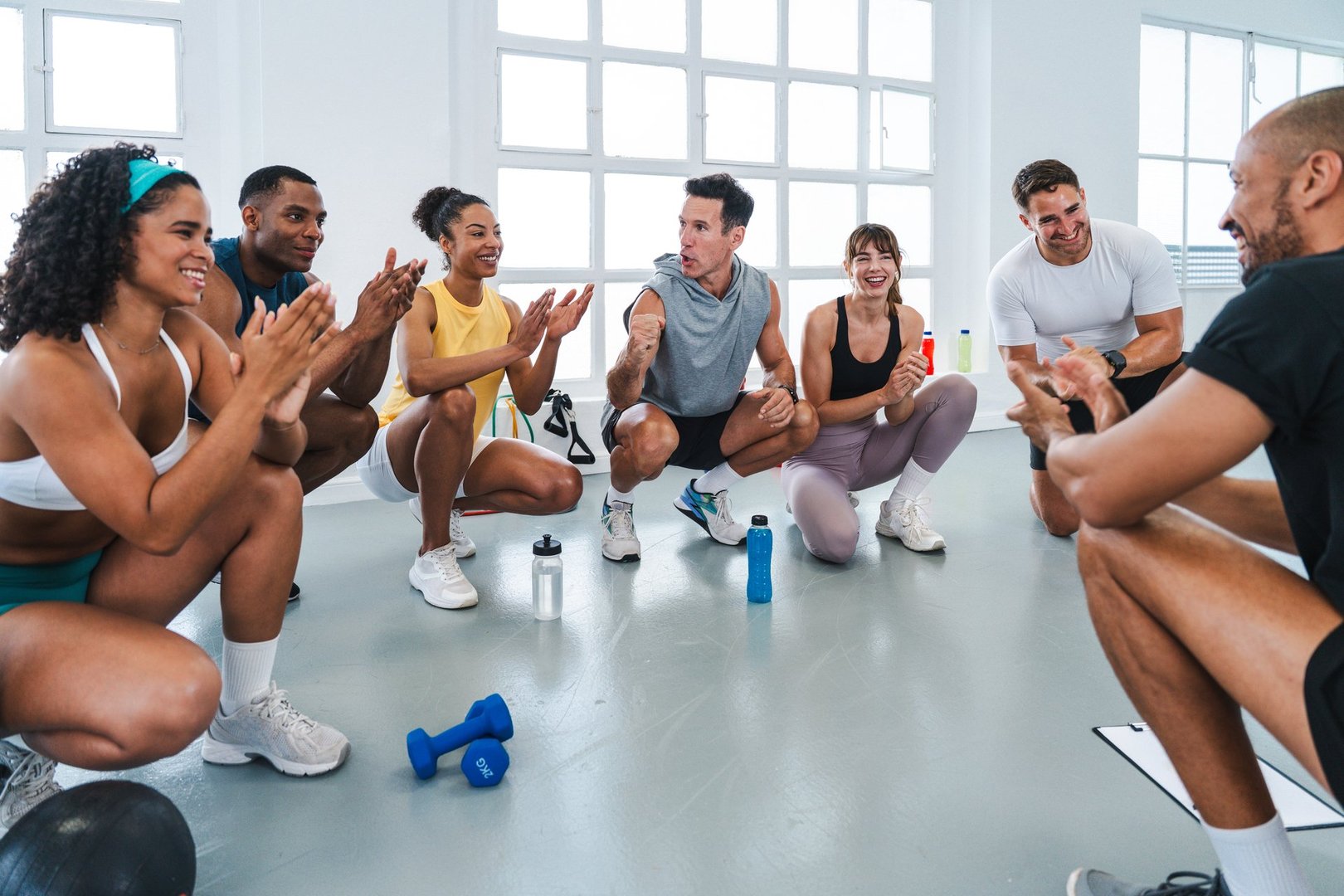 Multiethnic group of sportive people doing functional workout in training class gym motivated athletes clapping and celebrating with fitness trainer after completing intense functional training sessio