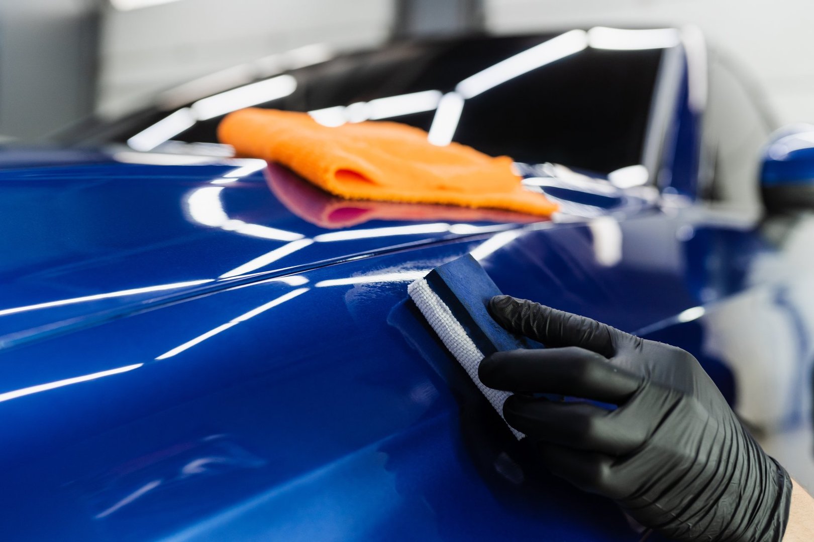 Process of applying ceramic protective coat on body car using sponge in detailing auto service. Car service worker apply ceramic coating to protect the car body from scratches