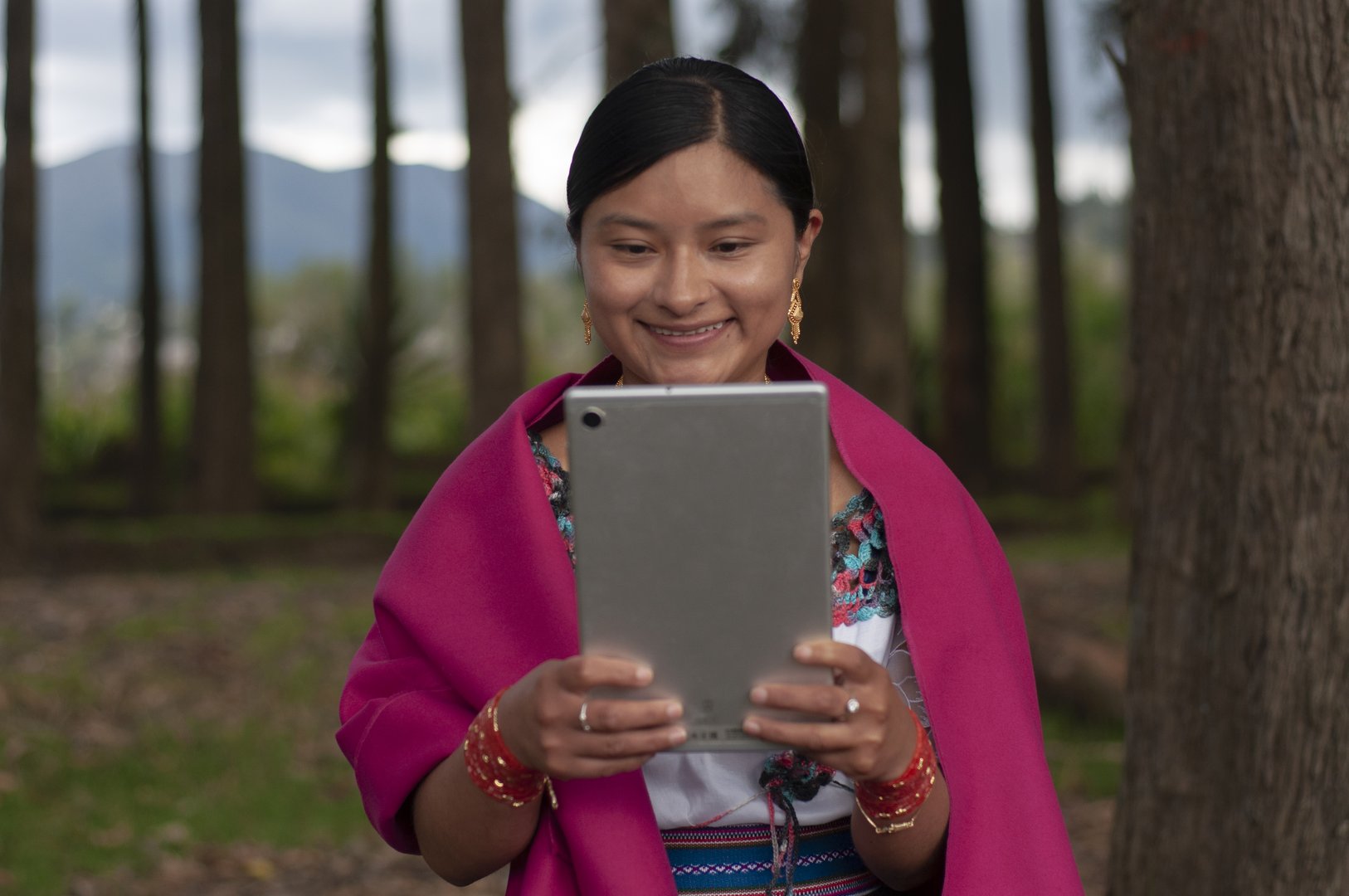 Indigenous woman from the Ecuadorian Amazon very happy and excited sitting in a forest with a tablet talking online with her friends