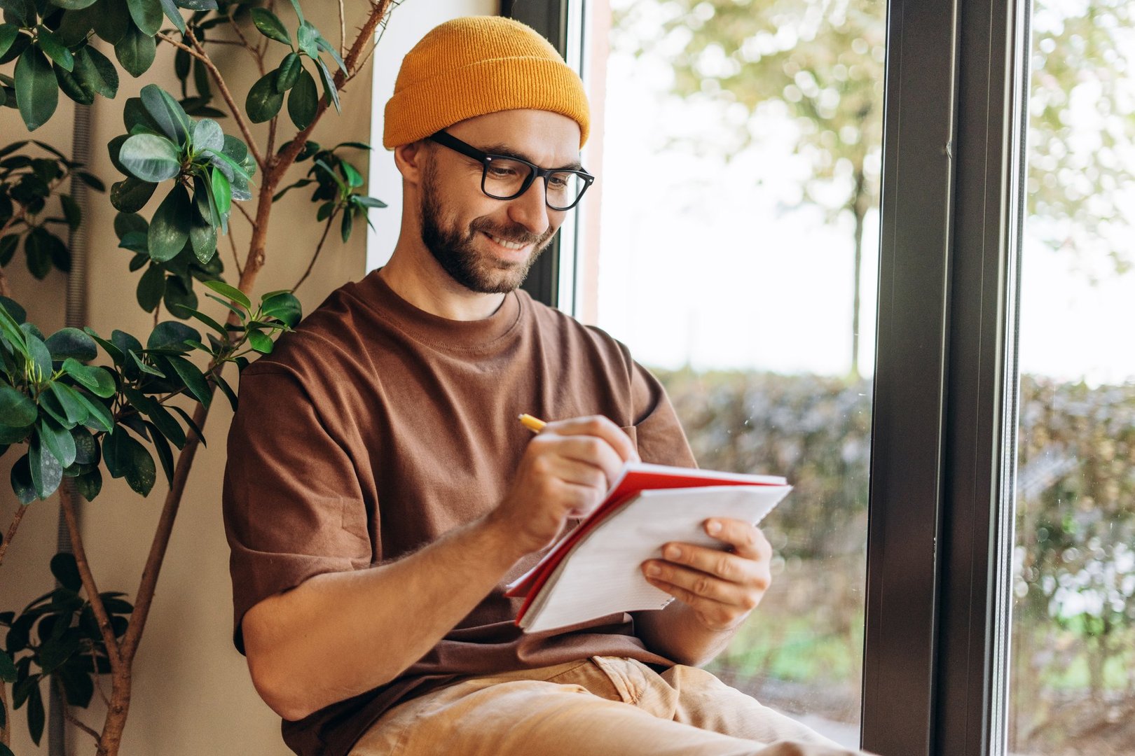 Portrait of smiling man wearing stylish eyeglasses taking notes, writing in notebook at home