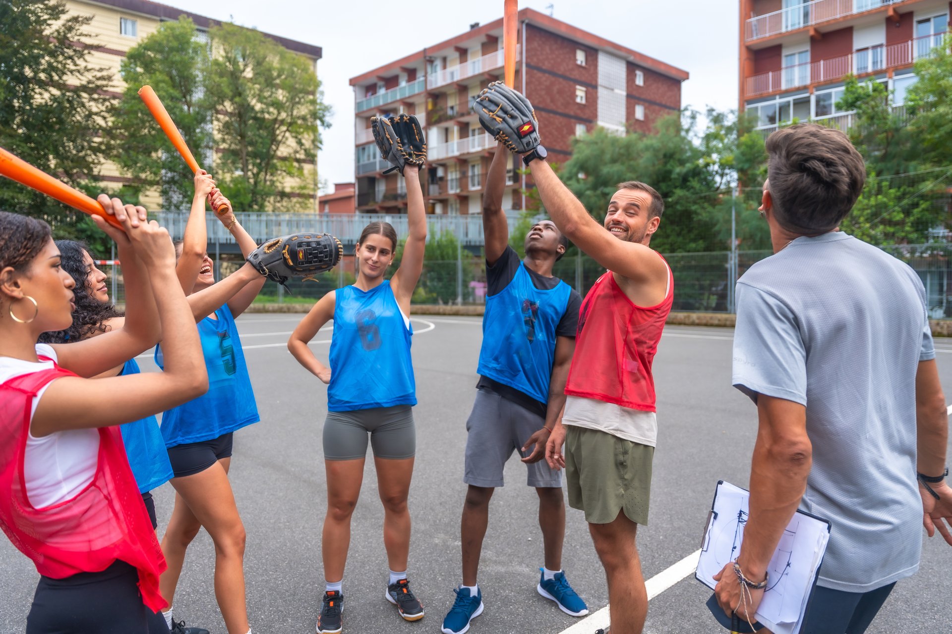 Multi-ethnic baseball team celebrating with their coach after a successful training session, giving high fives and holding bats and gloves, showing teamwork and sportsmanship