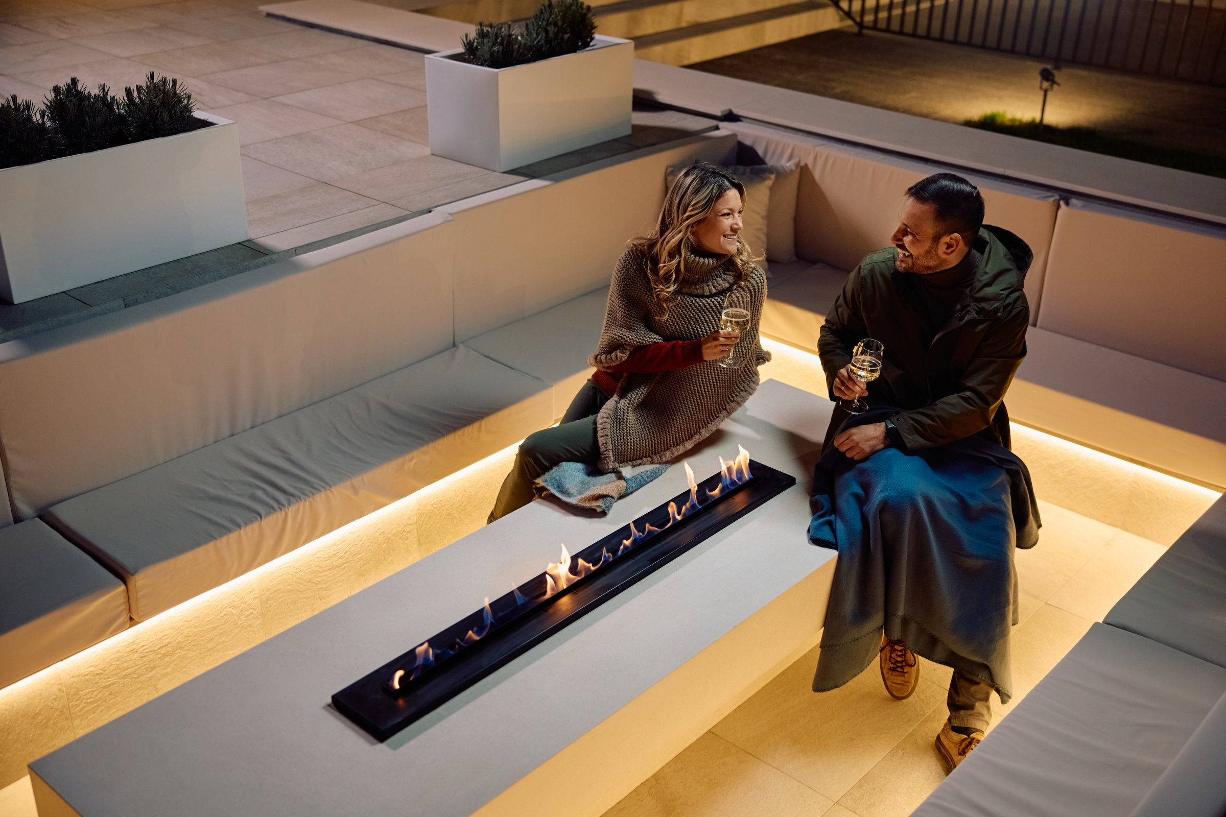 High angle view of happy couple enjoying in glass of wine while communicating by the fireplace on a patio in the evening. Copy space.