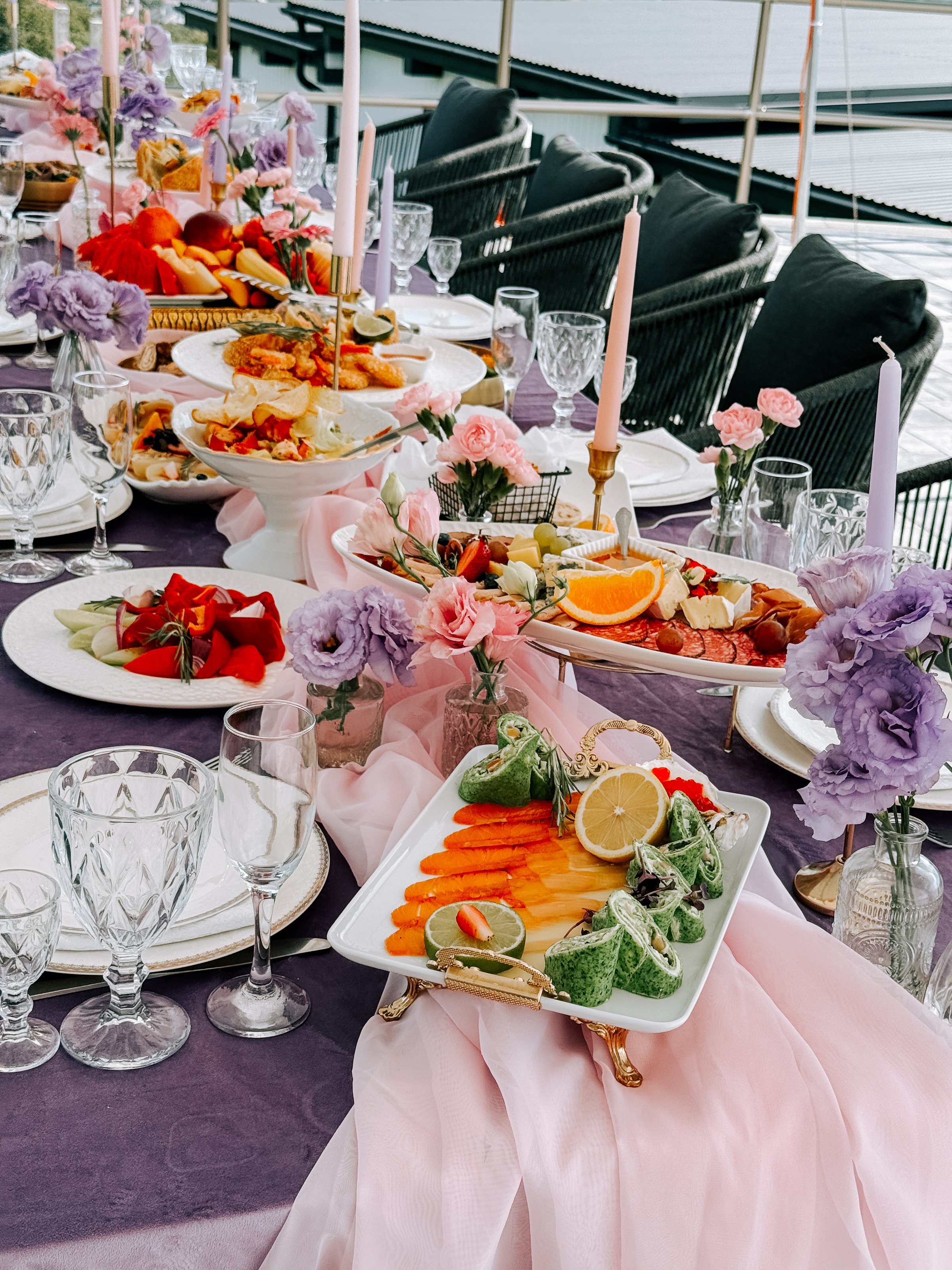 A beautifully arranged table showcases a variety of vibrant dishes, flowers, and candles by the water.