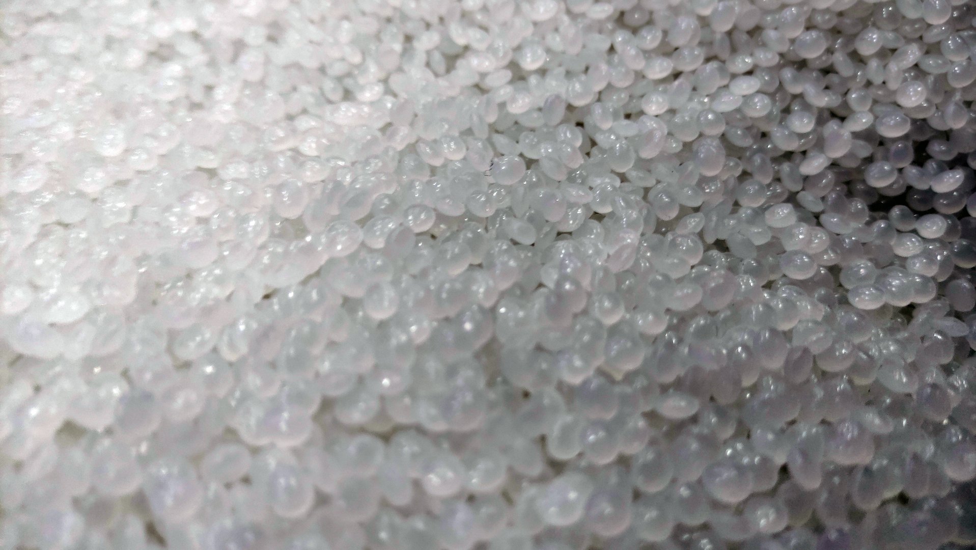 Macro image of clear plastic pellets used as raw material in plastic manufacturing and injection molding processes. The photo shows a dense cluster of translucent polymer granules with a smooth, rounded shape, typically used in the production of various plastic products. Ideal for illustrating concepts in industry, recycling, materials science, or manufacturing.