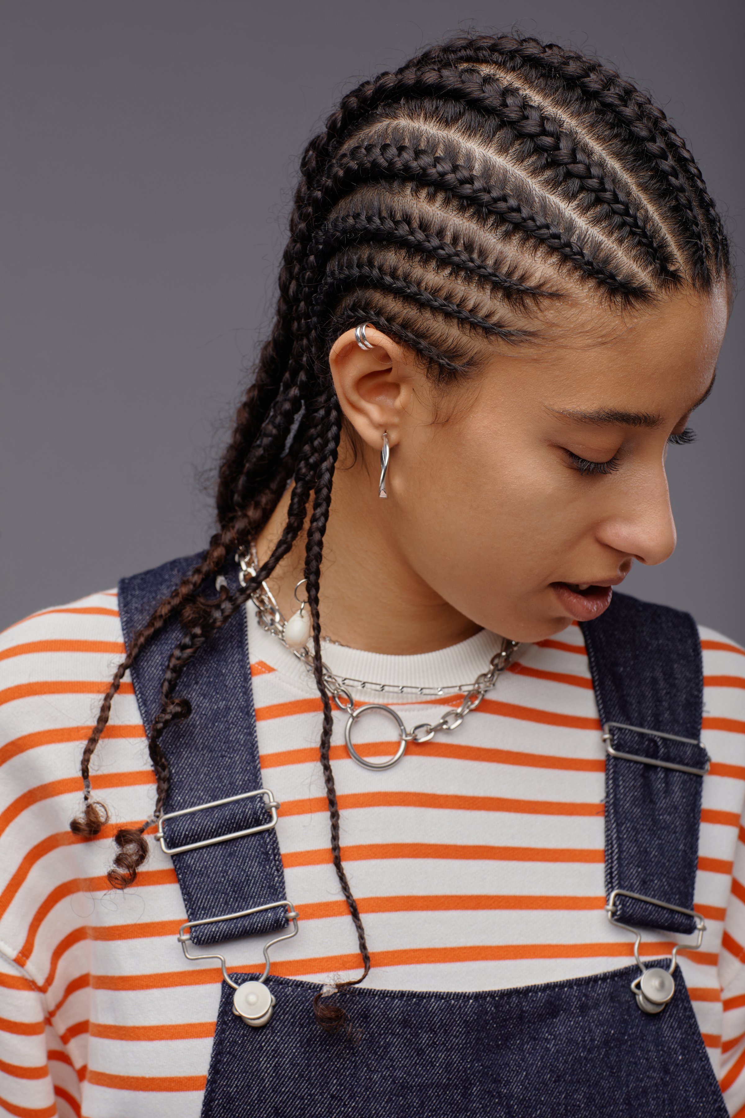 Minimal portrait of gen Z young woman with cornrows hairstyle looking away while posing on grey background in studio