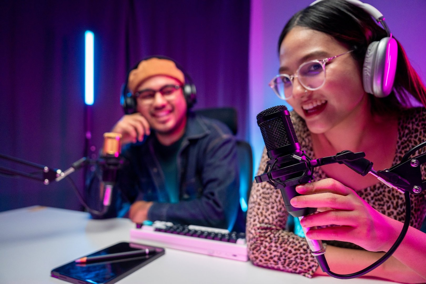 Young asian man and woman host streaming podcast with condenser microphone work on tablet at home broadcast studio. Content creator blogger recording voice over radio interview guest conversation