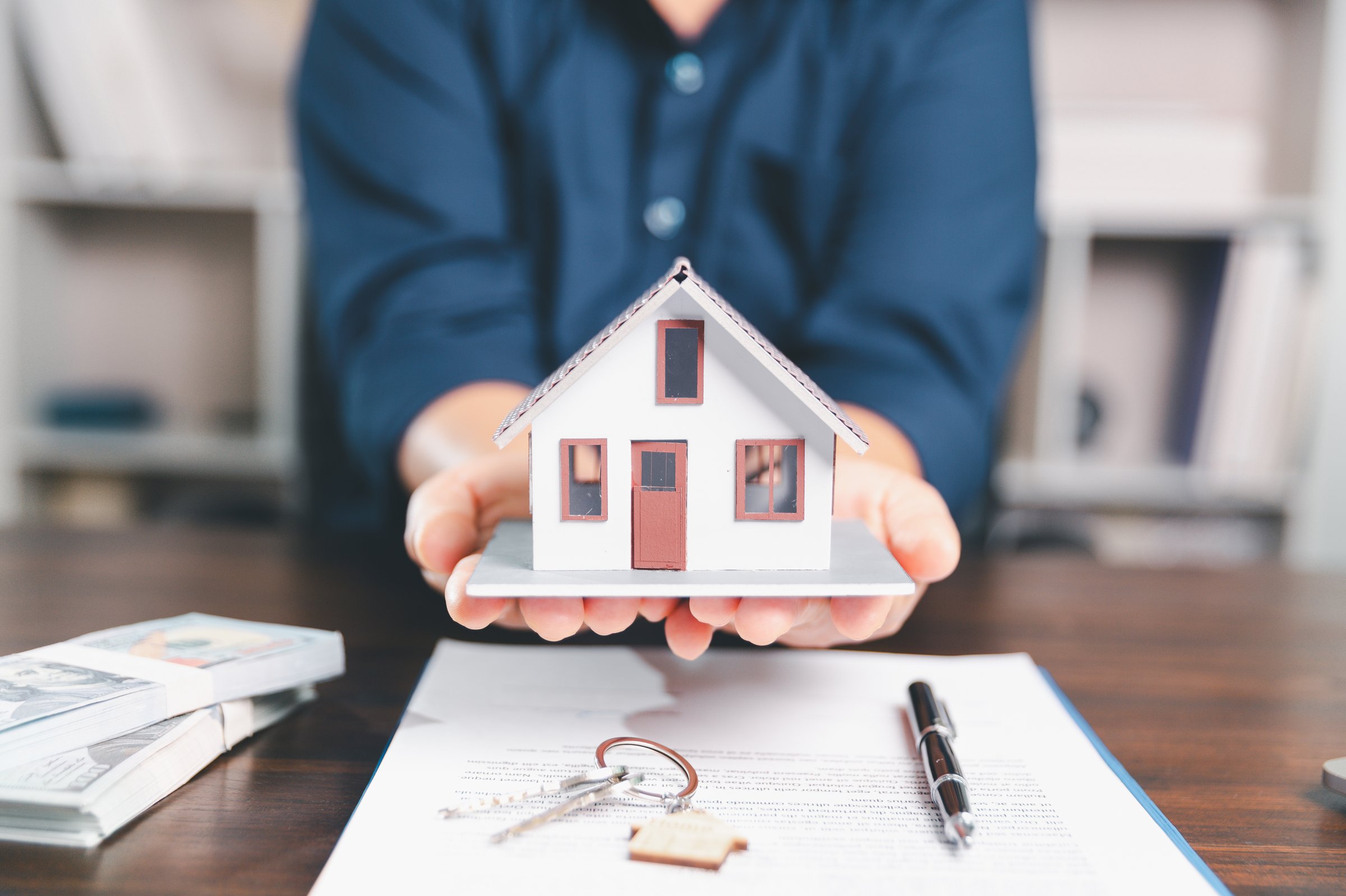 Model house, stacks of coins, calculator, financial documents on a wooden desk represent real estate investment and mortgage planning, highlighting financial growth and strategic planning strategies.