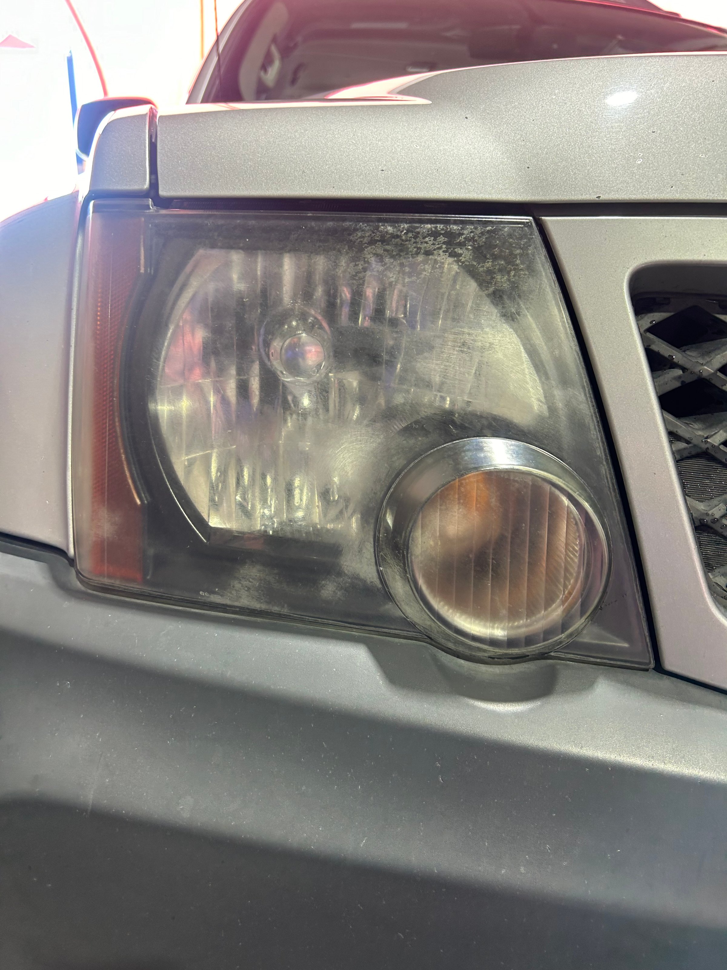 Close-up of a car's headlight showing dust and dirt on the lens and part of the front grille.