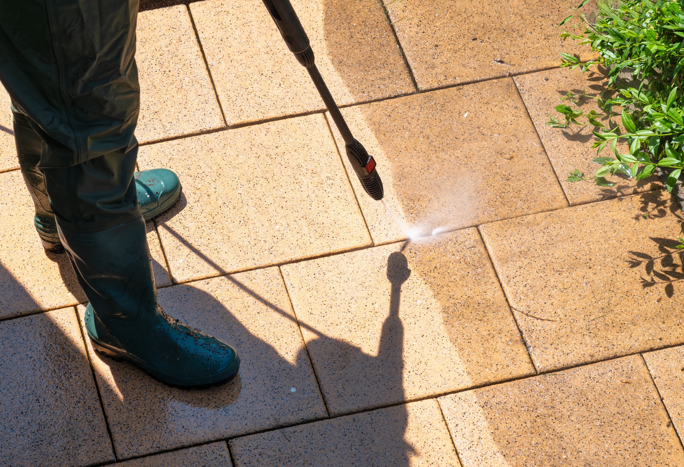 A person removes tough dirt from patio tiles using a high-pressure washer. Clear before-and-after effect
