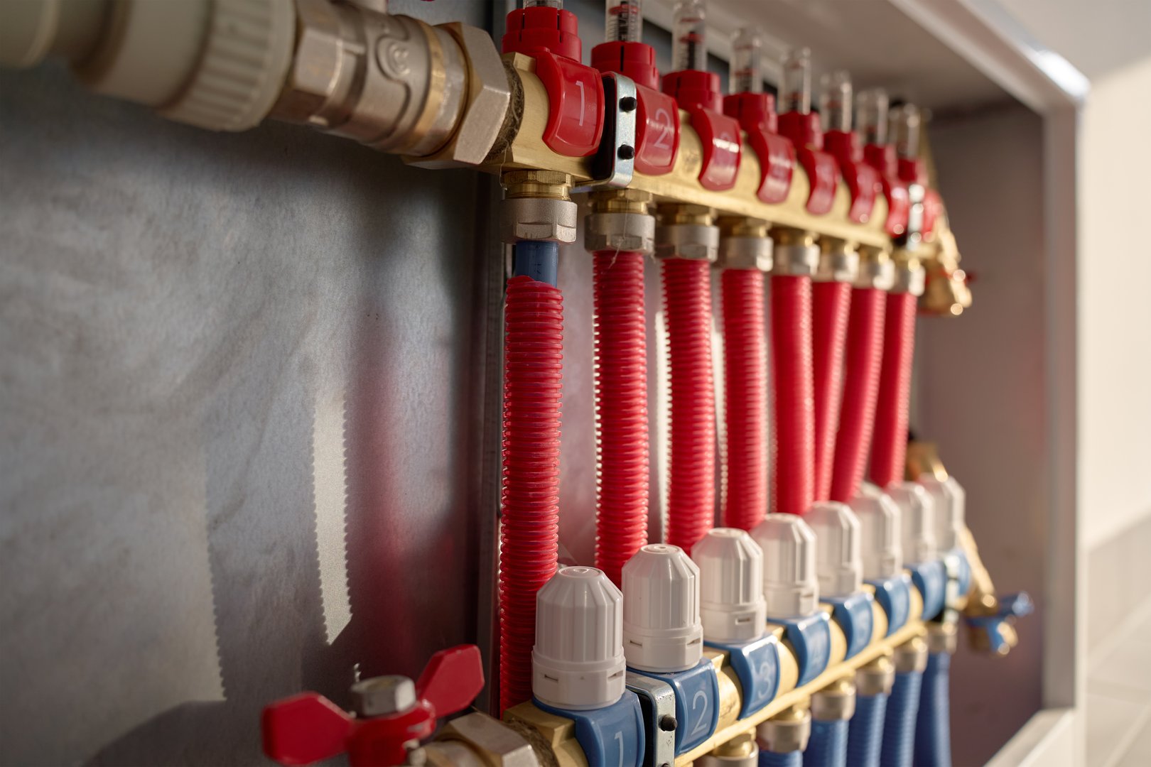 Underfloor heating manifold with control valves, flow meters and connected red pipes. Home heating system, plumbing and temperature control concept