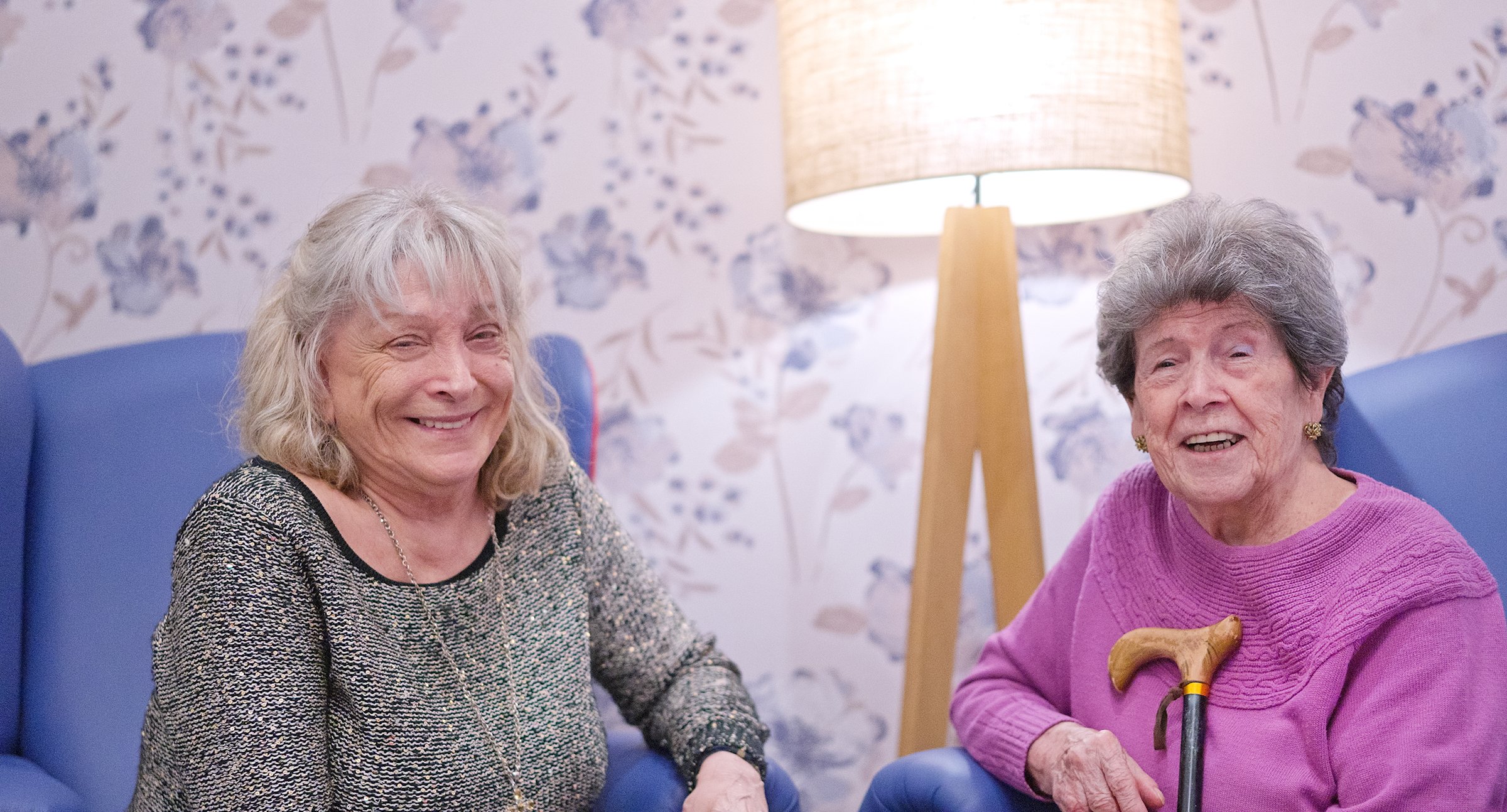 Two happy mature women sitting in armchairs, sharing a moment in a cheerful environment