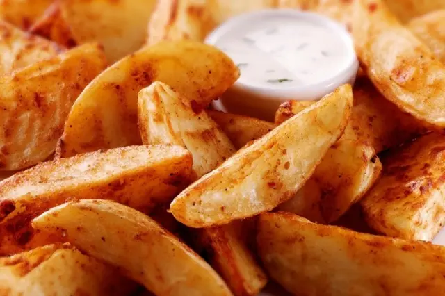 Close-up of seasoned potato wedges with a small cup of white dipping sauce in the background.