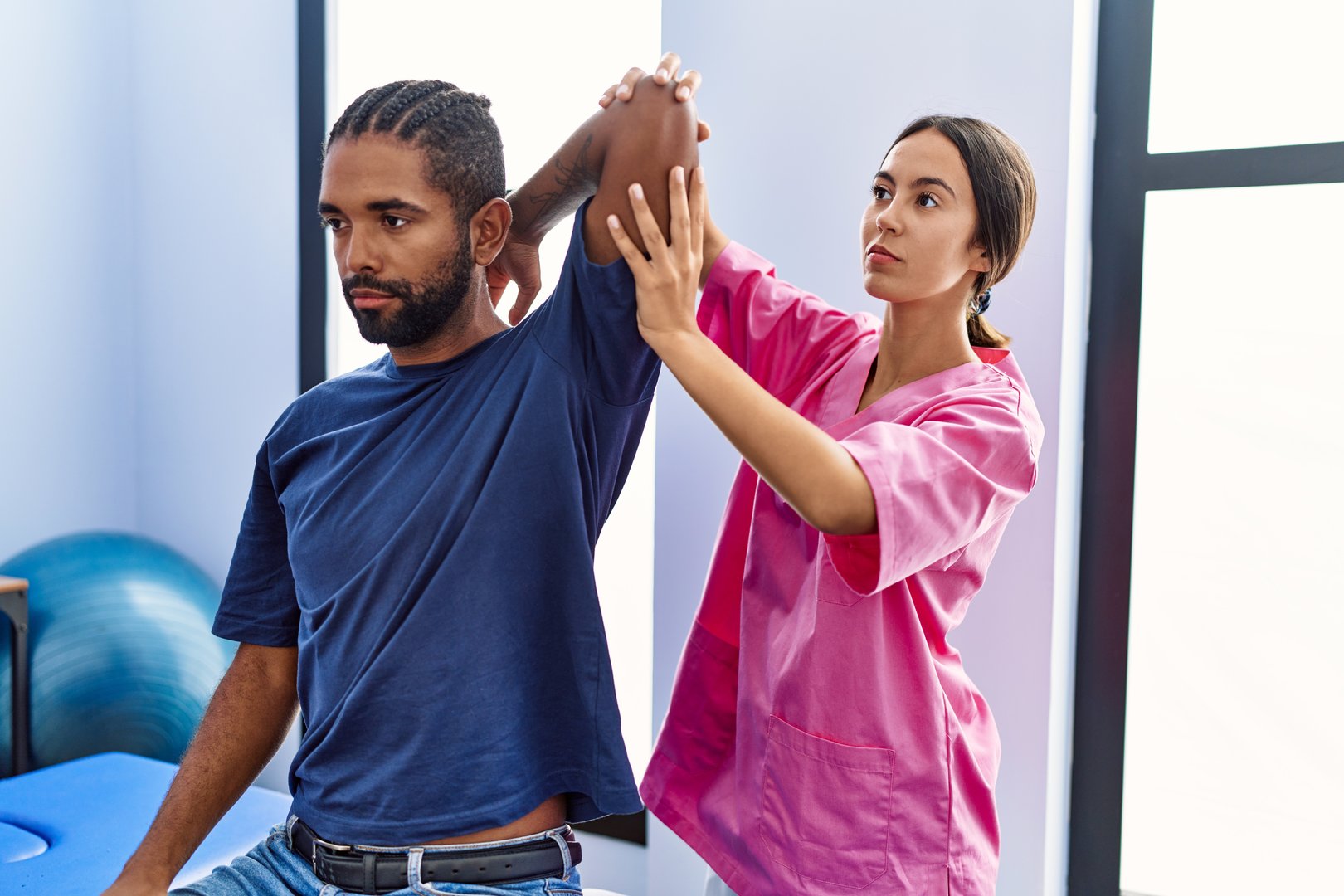 Man and woman wearing physiotherapist uniform having rehab session stretching arm at physiotherpy clinic