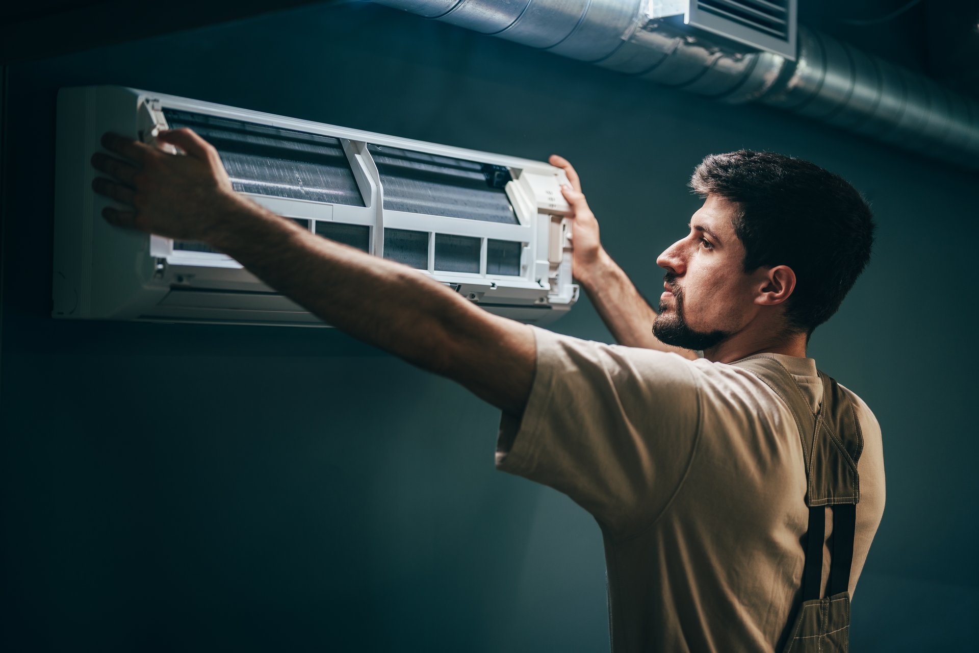 A technician works diligently to install an air conditioning unit in a home. Tools are organized nearby, and the setting is well-lit with natural light coming in from a window.