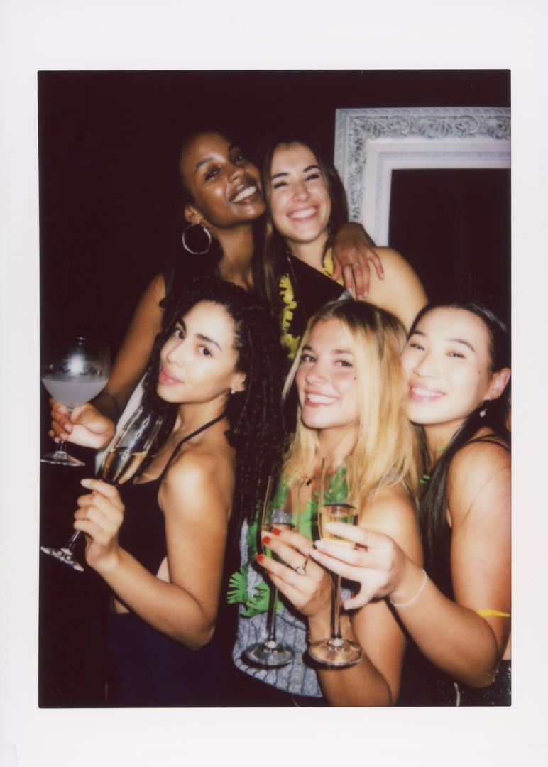 A joyful group of friends happily celebrating with drinks, captured in an instant camera photo. The image has a vintage feel with visible dust and scratches, enhancing the nostalgic vibe.