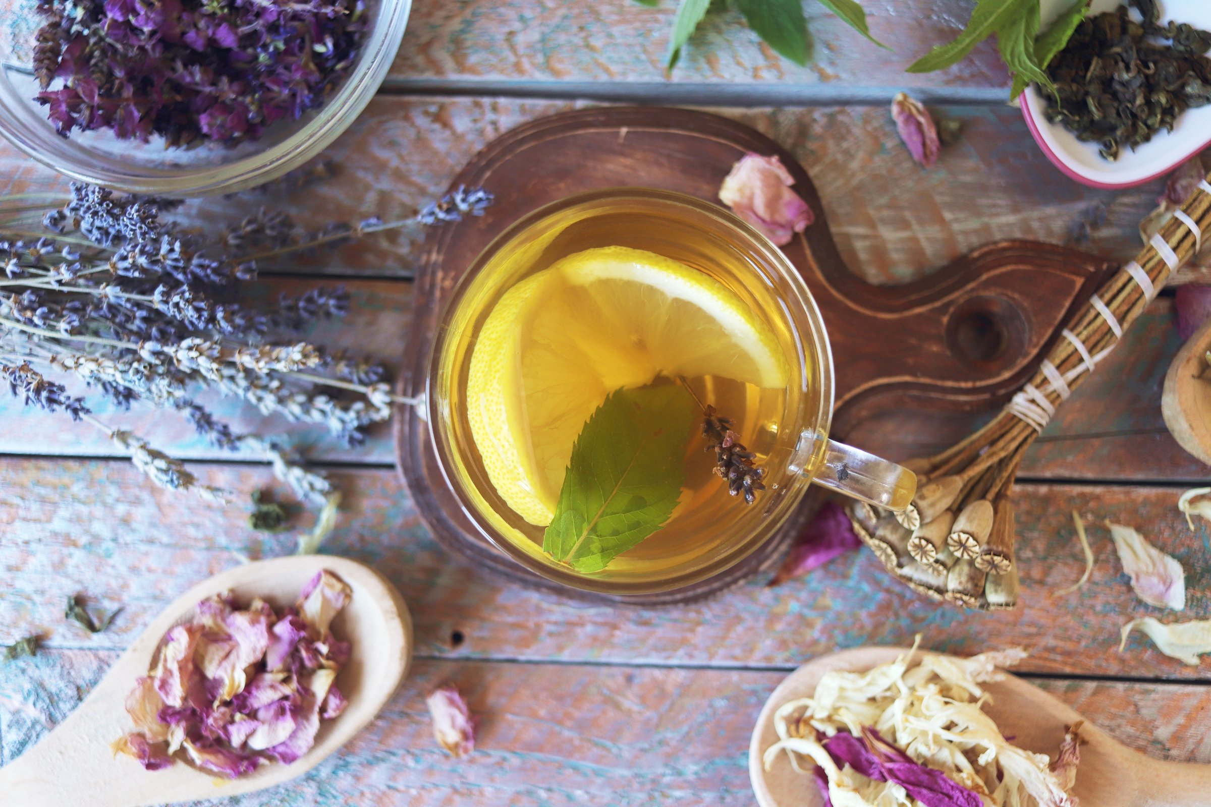 Cup of green tea with mint and lemon, dry petals of useful plants on a wooden table