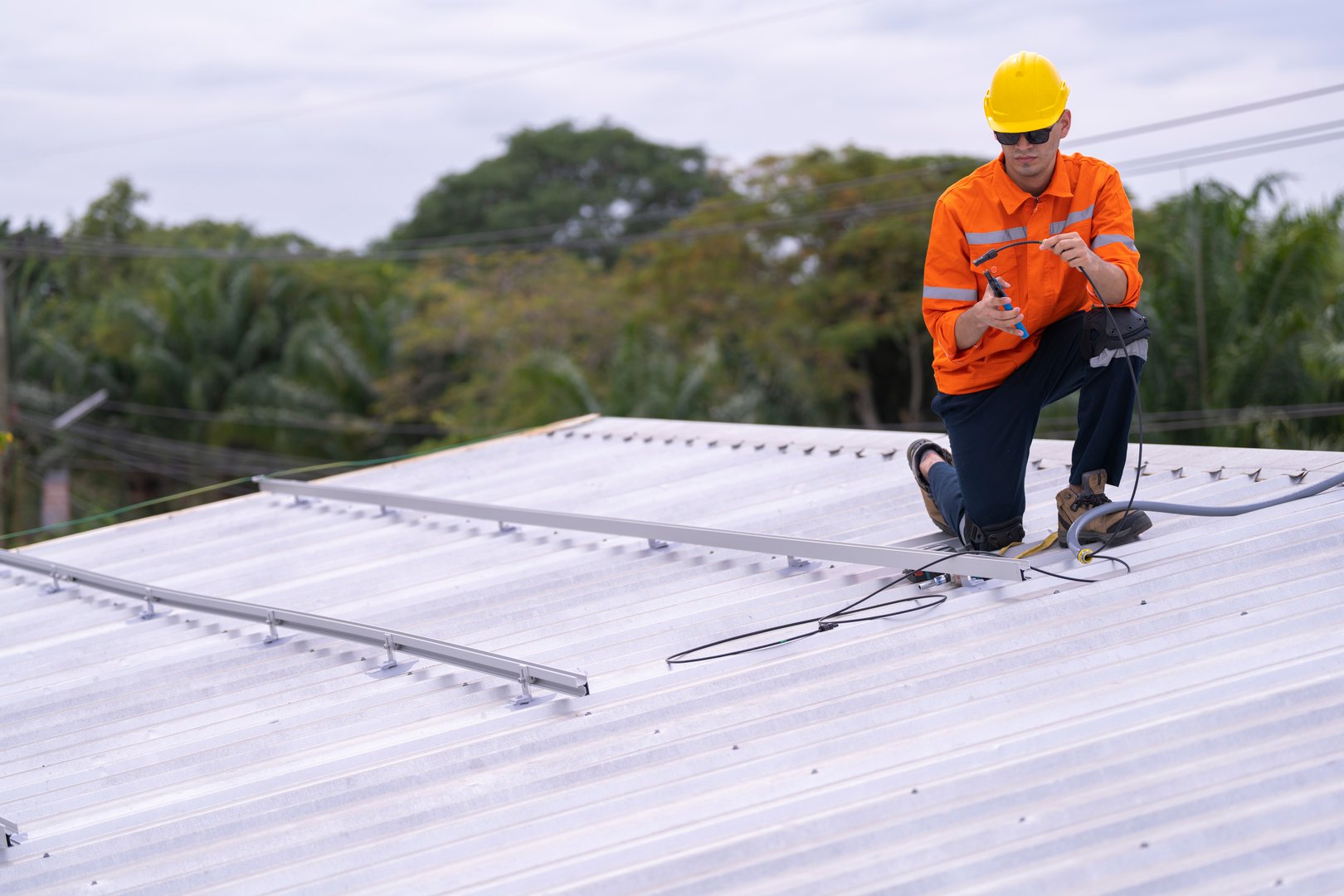Technician in an orange safety uniform and helmet handling an electrical cable on a rooftop. Represents safety, professionalism, and expertise in renewable energy installations and maintenance work.