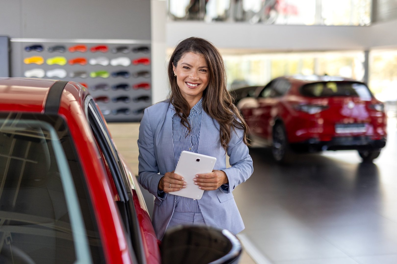Portrait of a female car saleswoman working in the showroom. Close up of a businesswoman standing next to car in the showroom. Female manager in car dealership