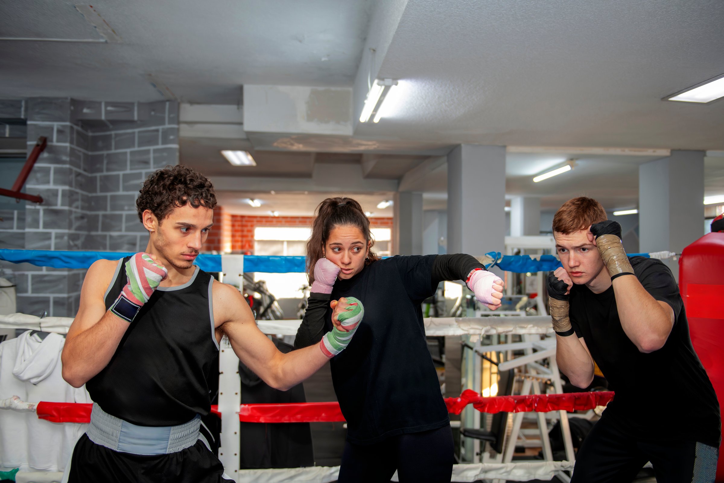 Three young boxers training inside a boxing ring, practicing their punches and defensive moves