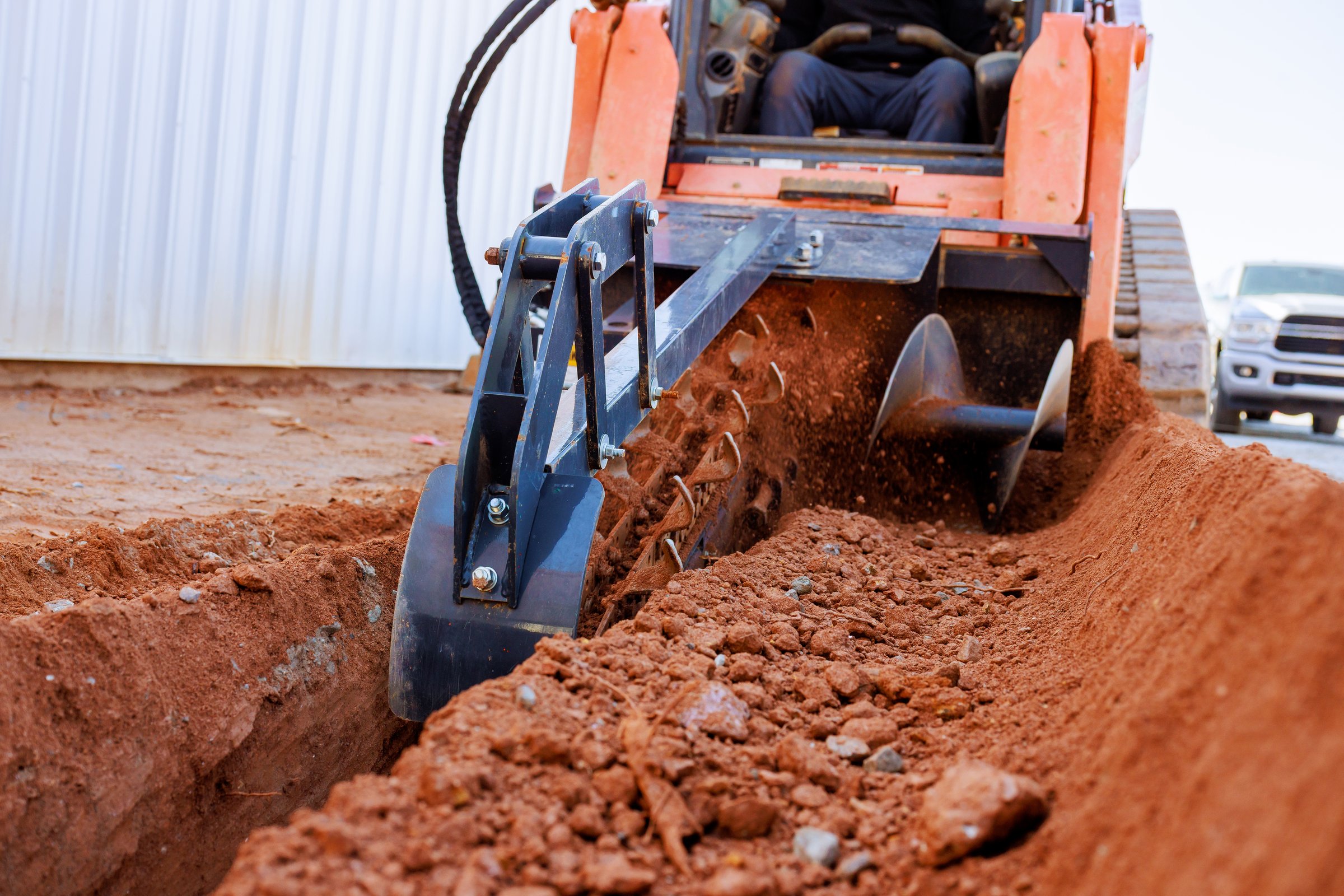 Trencher cuts through soil as worker prepare for underground utility installation in construction area