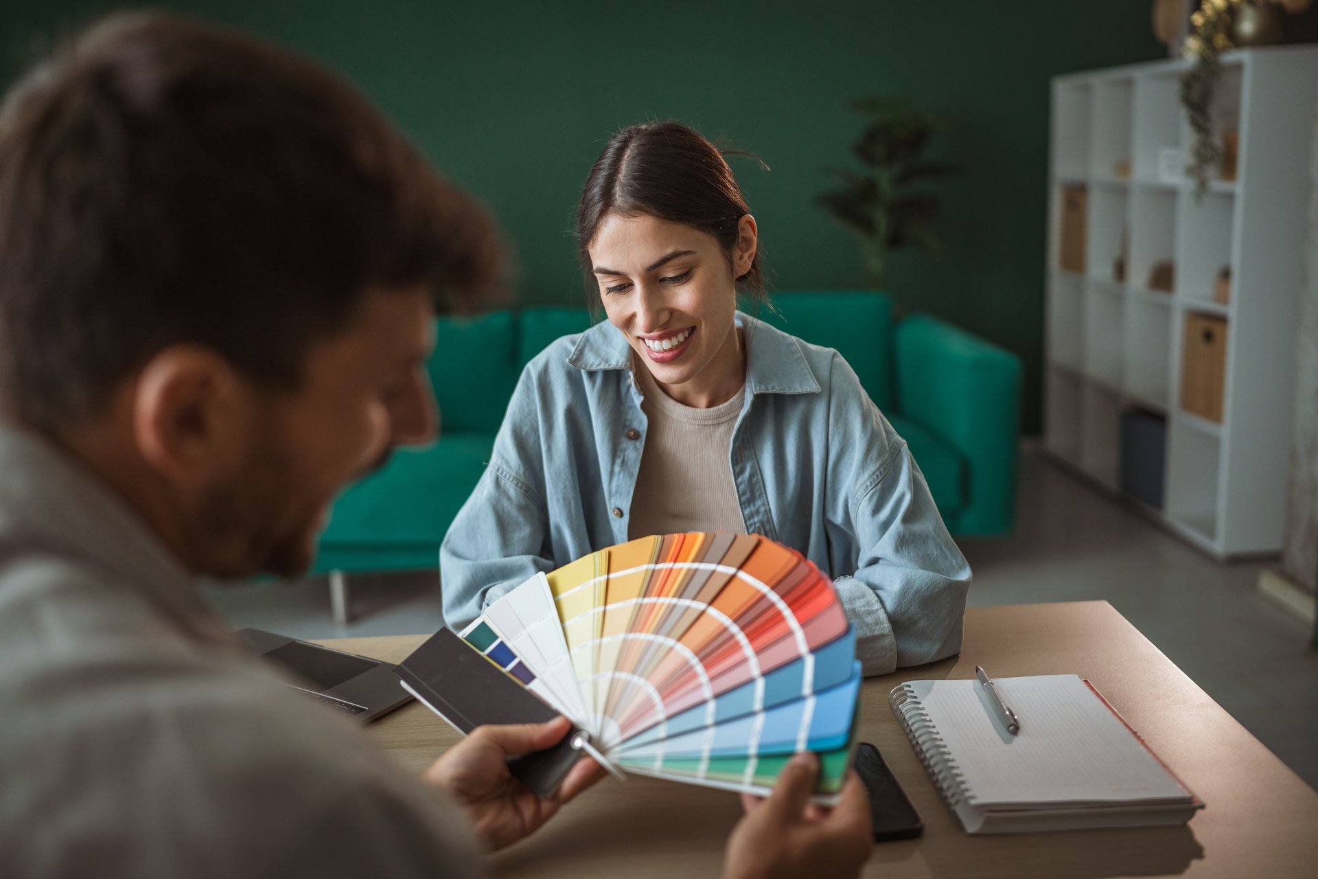 Young female interior designer sitting at a desk and smiling, discussing color choices and home renovation plans with a client during a professional consultation