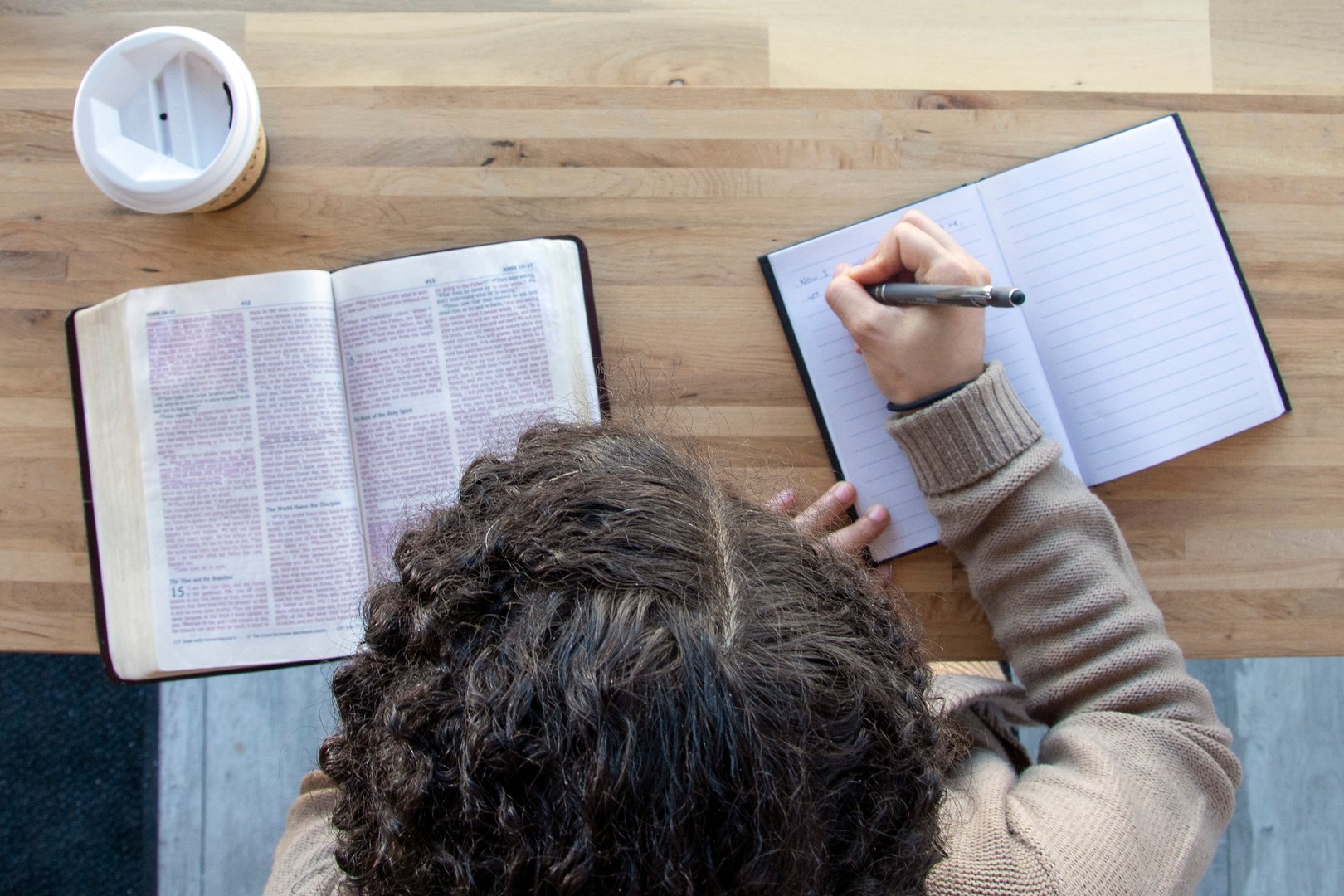 black woman sits and studying her bible with journal while drinking coffee