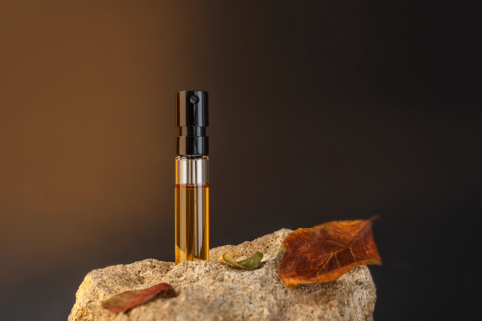 Beautiful glass sprayer bottle standing on a stone with apple leaves. Autumn cosmetic concept composition. Wooden scent perfume sample presentation. Luxury product advertising concept or mockup