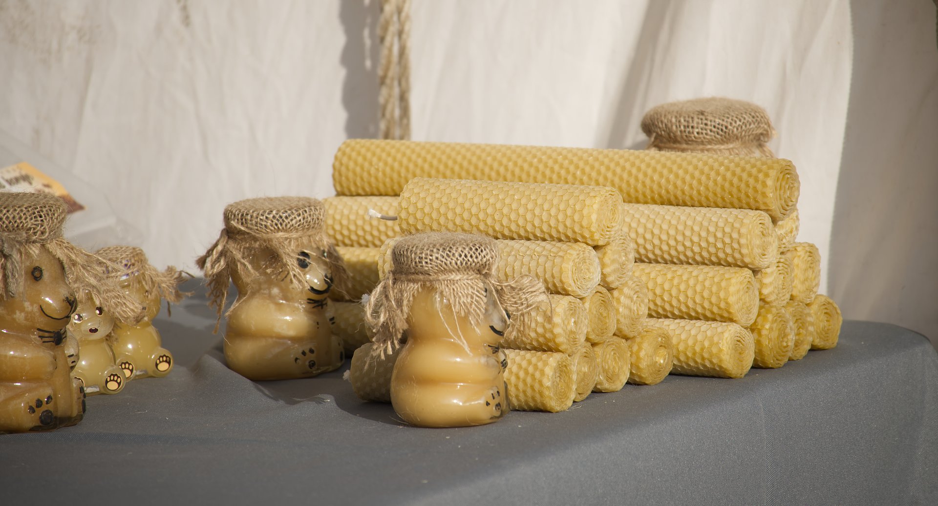 Handmade wax candles with a honeycomb pattern and decorative jars filled with honey are displayed at market stall showcasing traditional craftsmanship and natural materials in an artistic arrangement