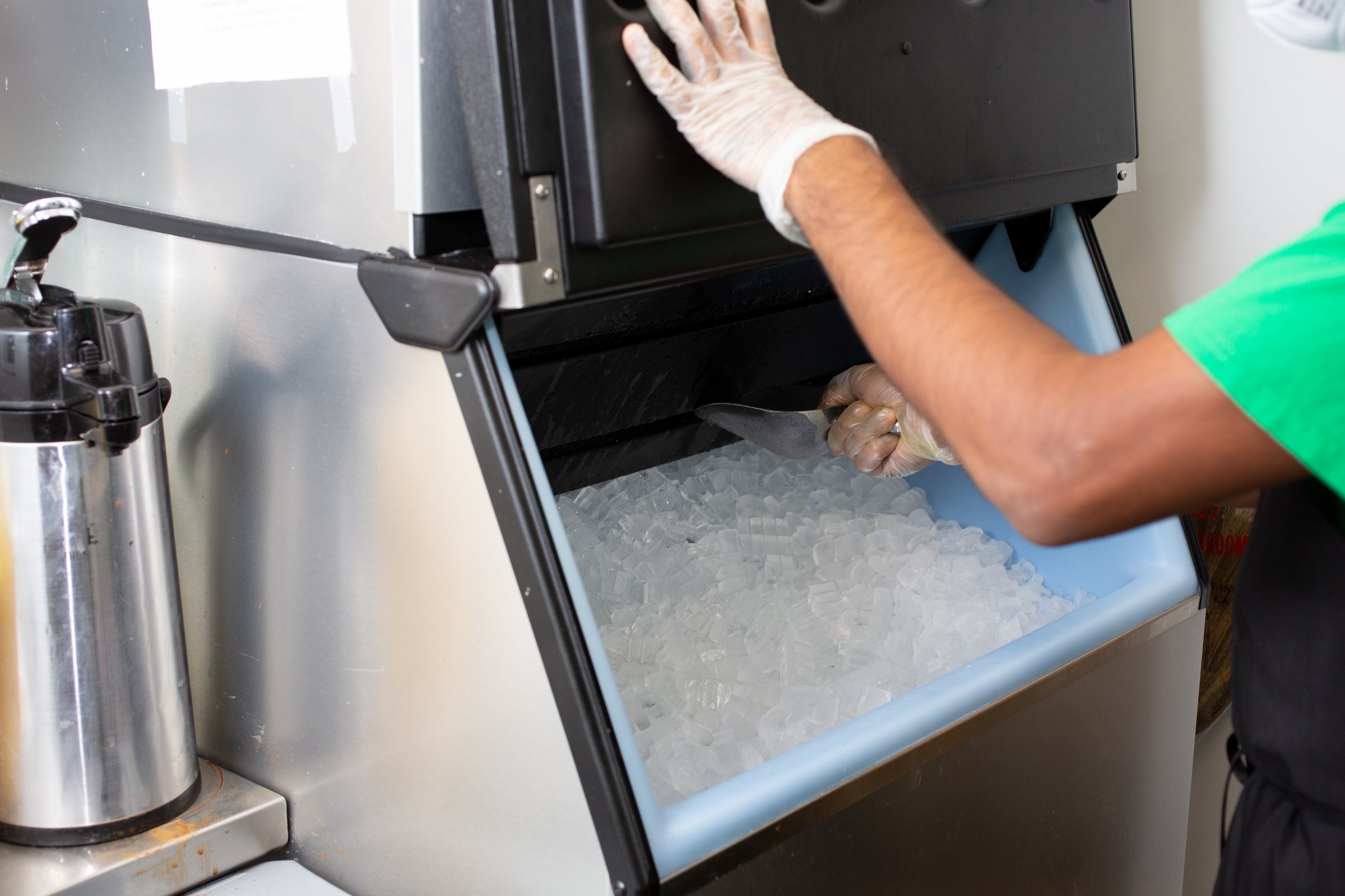 A view of an employee scooping ice out of an ice machine, in a restaurant setting