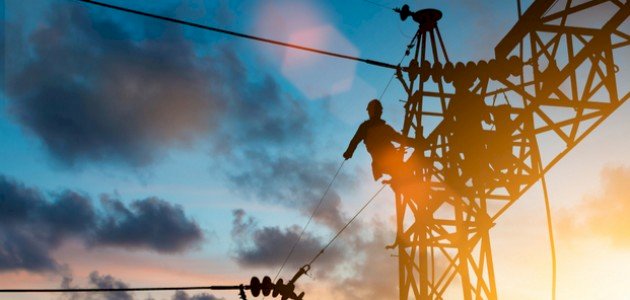 Silhouette of a worker climbing a power line tower at sunset with clouds in the sky.