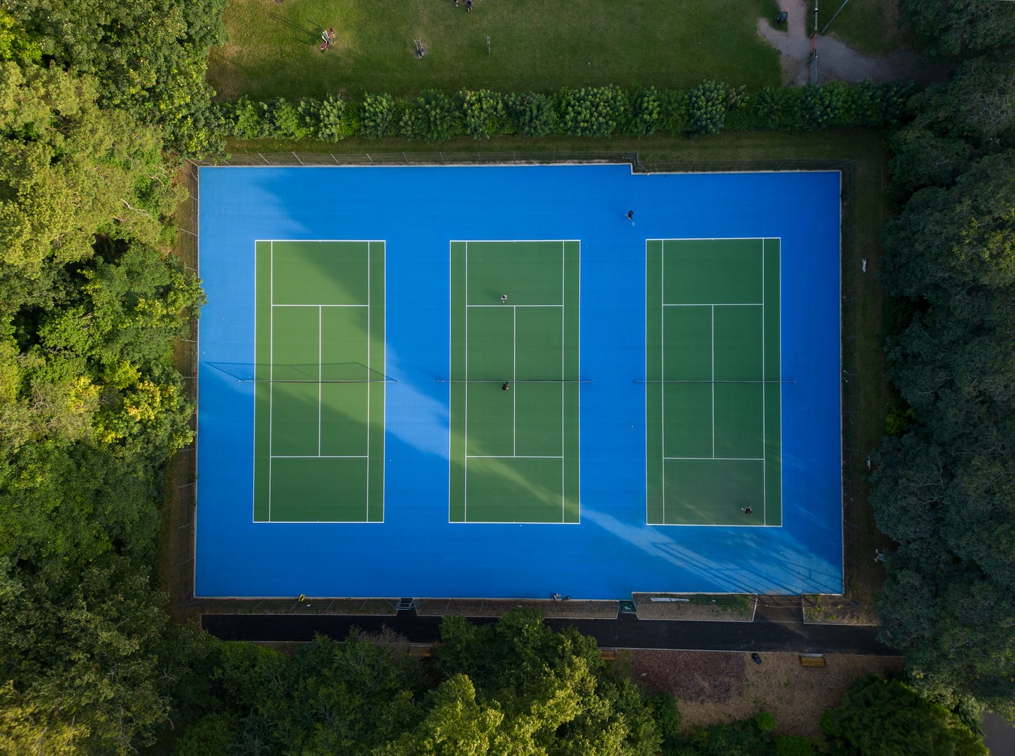 Tennis court at Swindon Town Gardens at sunset. Aerial top town view of recreational grounds with people playing tennis. Tall botanical trees offer a shade in the summer. Peaceful and safe green environment.