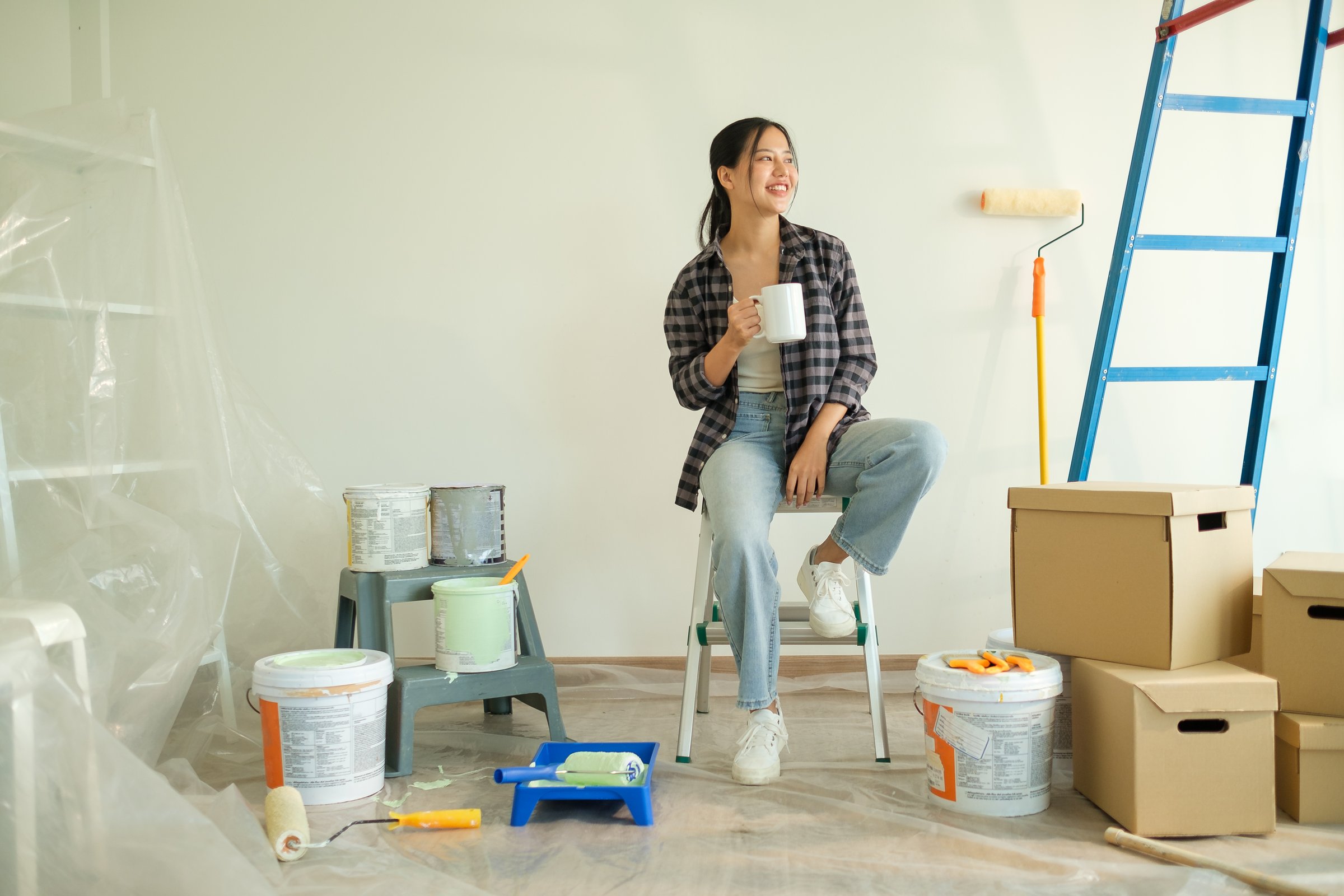 Attractive young woman taking a break during a home renovation project, sitting on the floor surrounded by painting supplies.