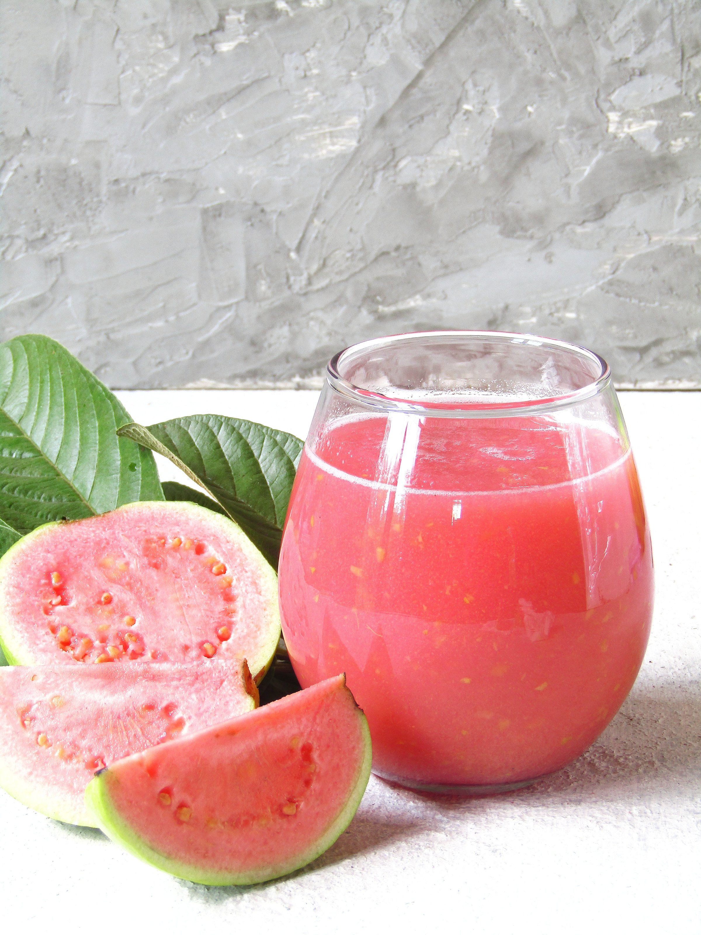 Guava juice in a bubble glass, decorated with guava fruit and leaves, on a light gray board