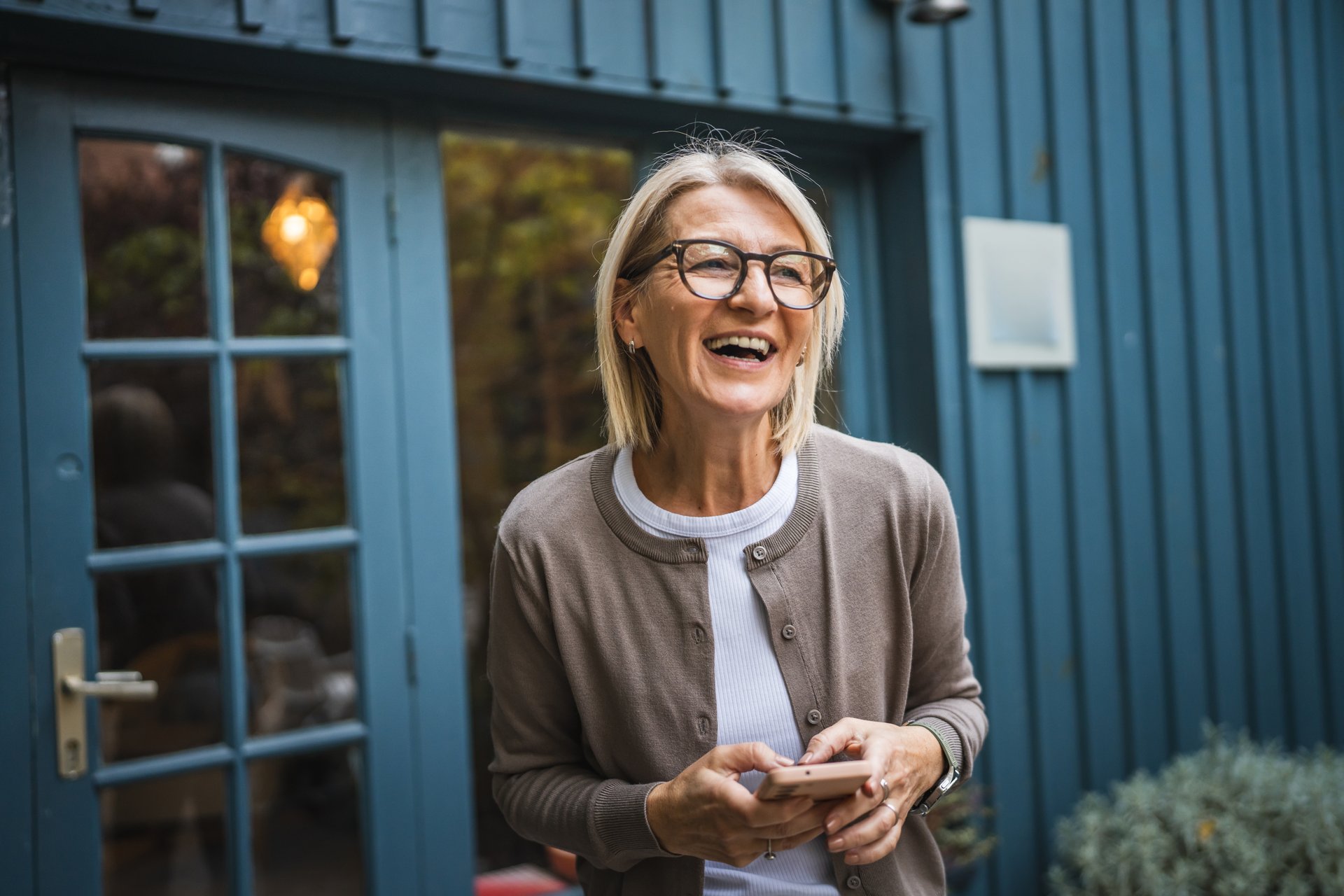 smile mature woman owner waitress stand in front restaurant and use mobile phone