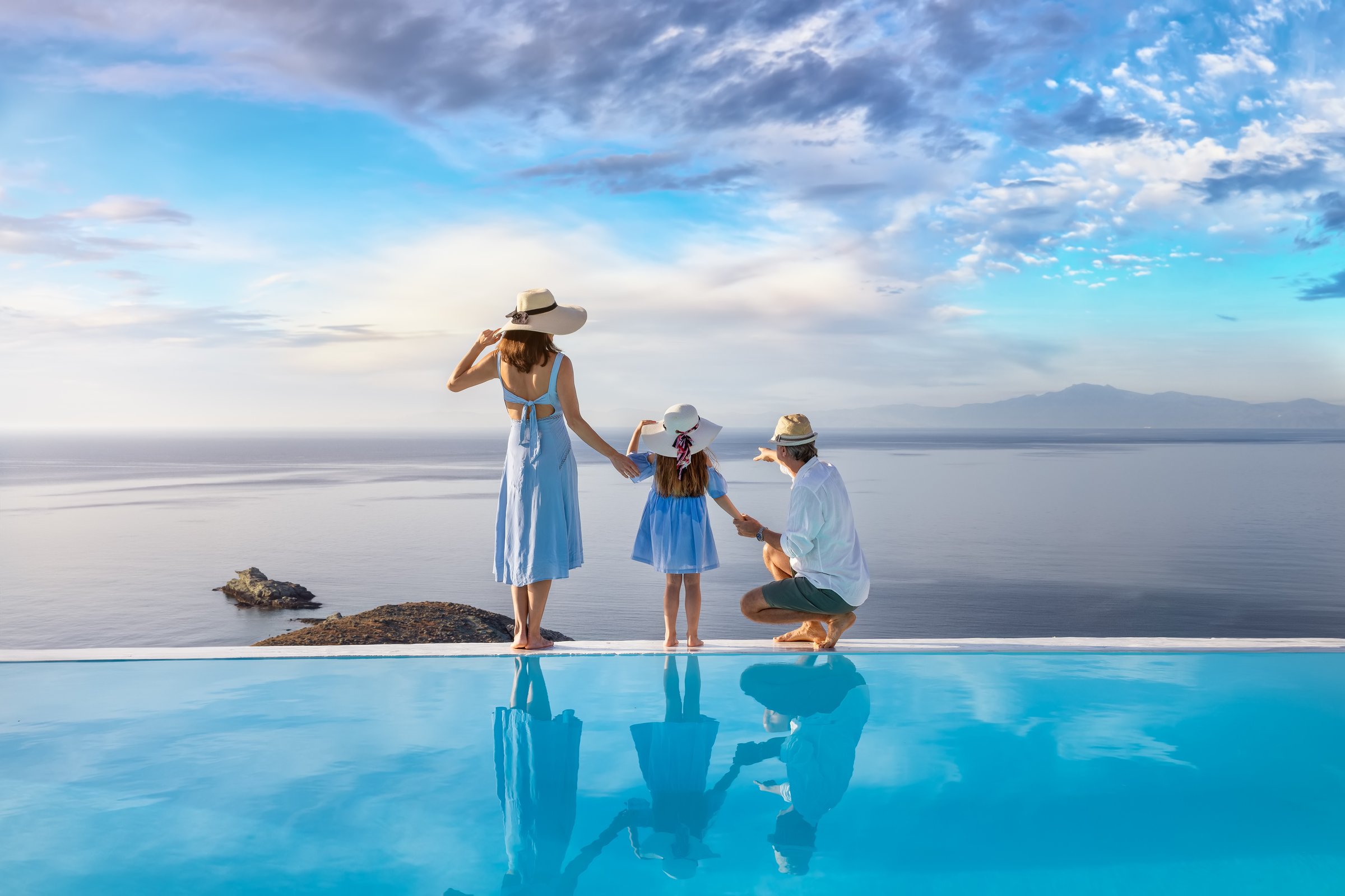 A beautiful family stands at the edge of a swimming pool and enjoys the view over the ocean during their holidays