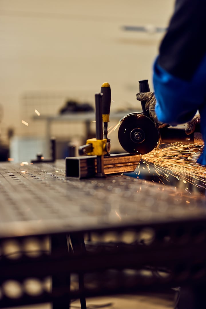 A worker uses a grinder on metal inside an industrial workshop, producing bright sparks
