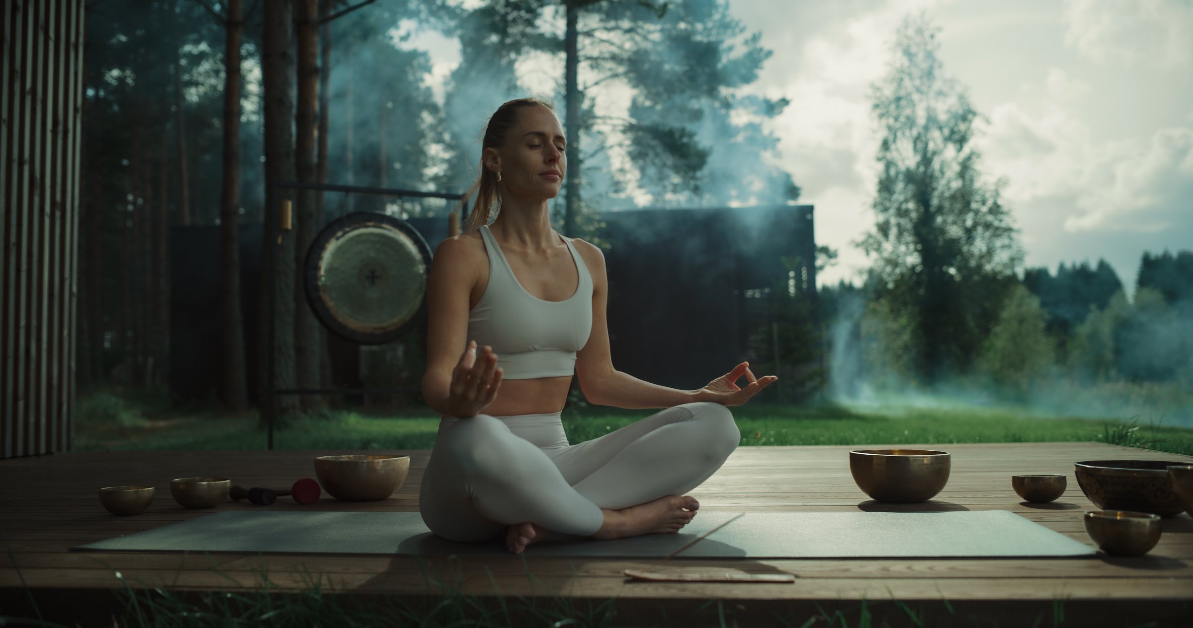 With a Gong in the Background and Trees Surrounding Her, a Young Female Meditates on Terrace, Incense and Singing Bowls Placed Nearby. Aromatic Scents and Peaceful Sounds Enhance the Mindfulness