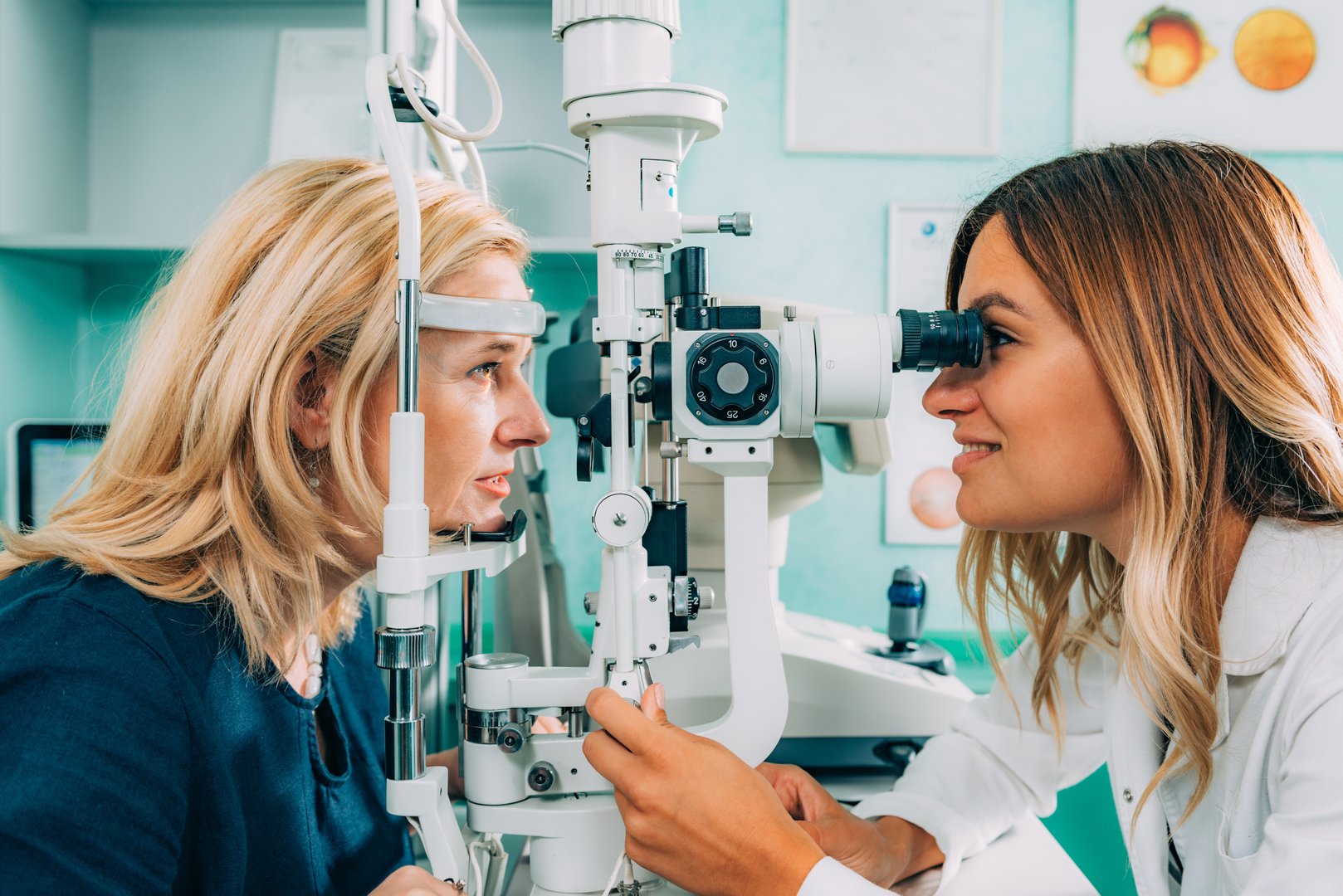 An optometrist examines a patient's eyes using a slit lamp in a clinical setting.
