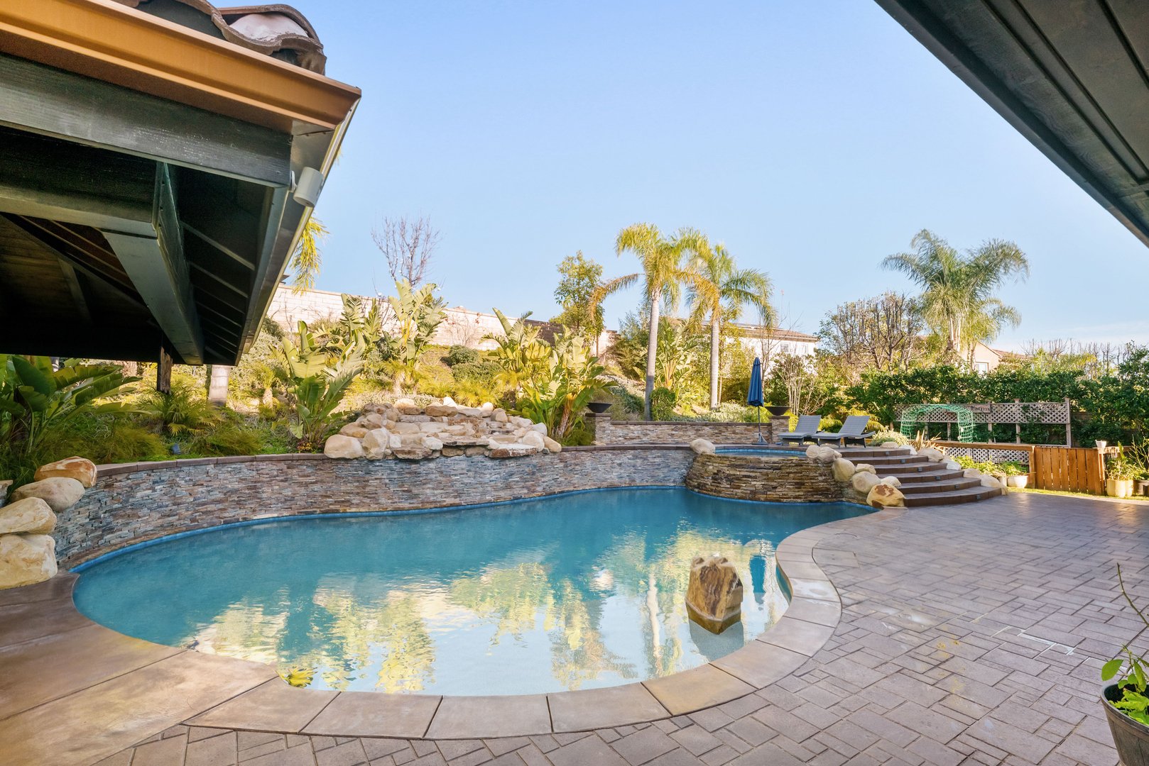 A luxury outdoor living space with covered patio, pool, lush landscaping, and stone accents