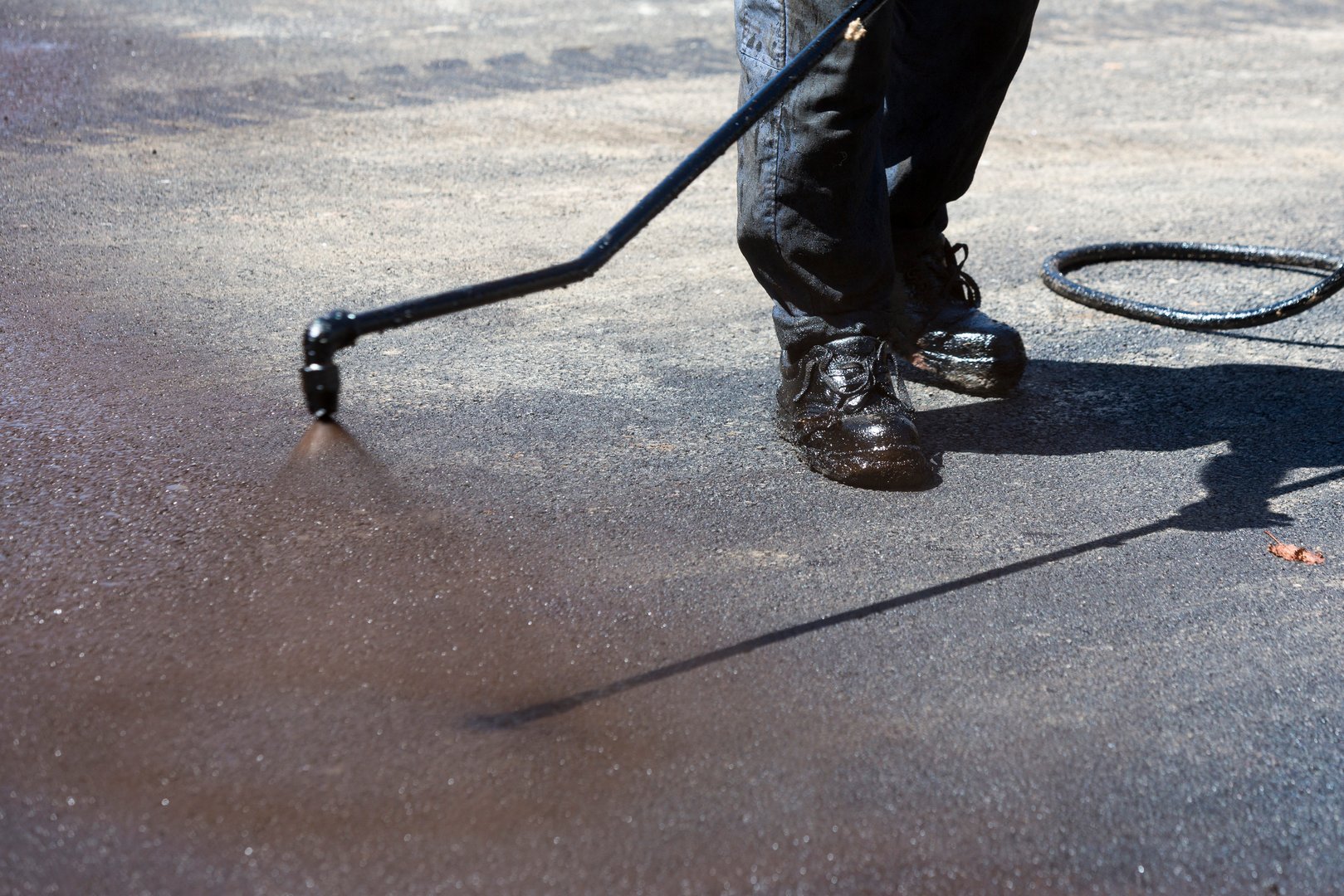Worker is spraying the black hot asphalt at a road construction.