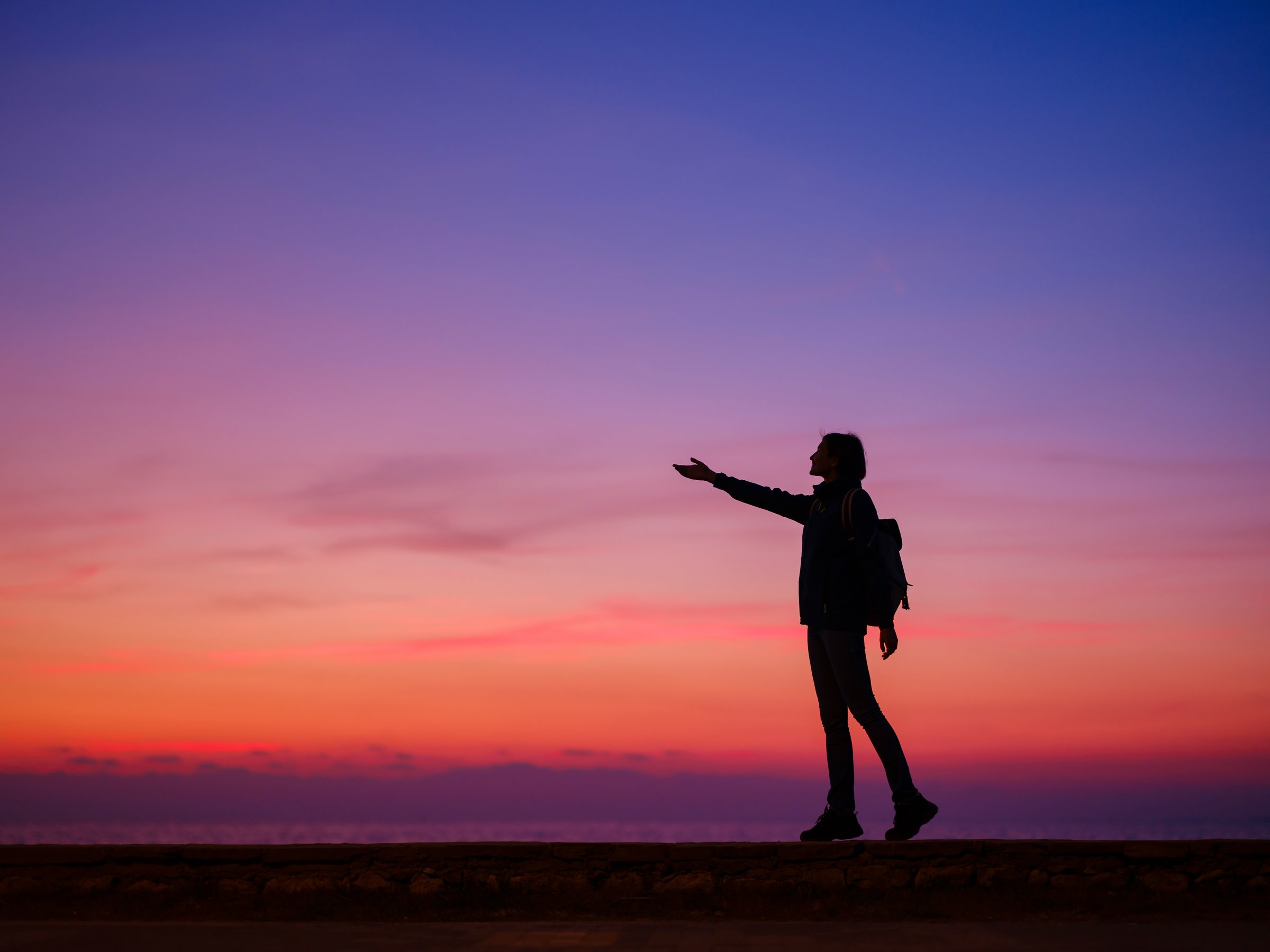 Woman tourist against colorful sunset sky. Travel, tourism concept. Active lifestyle and success idea gesture.