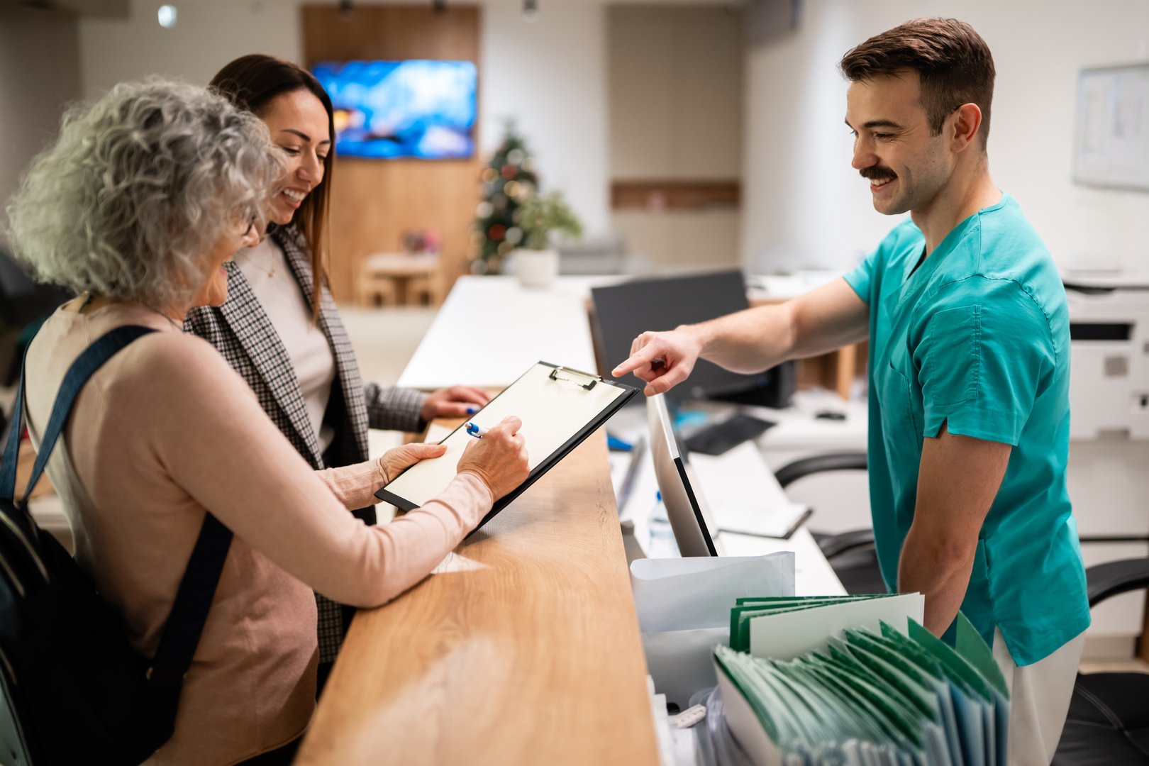 Medical staff assisting a senior patient and woman completing paperwork at the hospital check-in desk, providing healthcare service