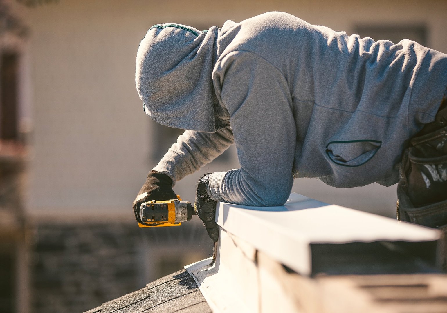 A roof repairman installs a metal ridge cap on top of a roof to seal and protect the roofline during maintenance. He is working with tools and safety gear under clear daylight, ensuring the roof's durability and weather resistance.