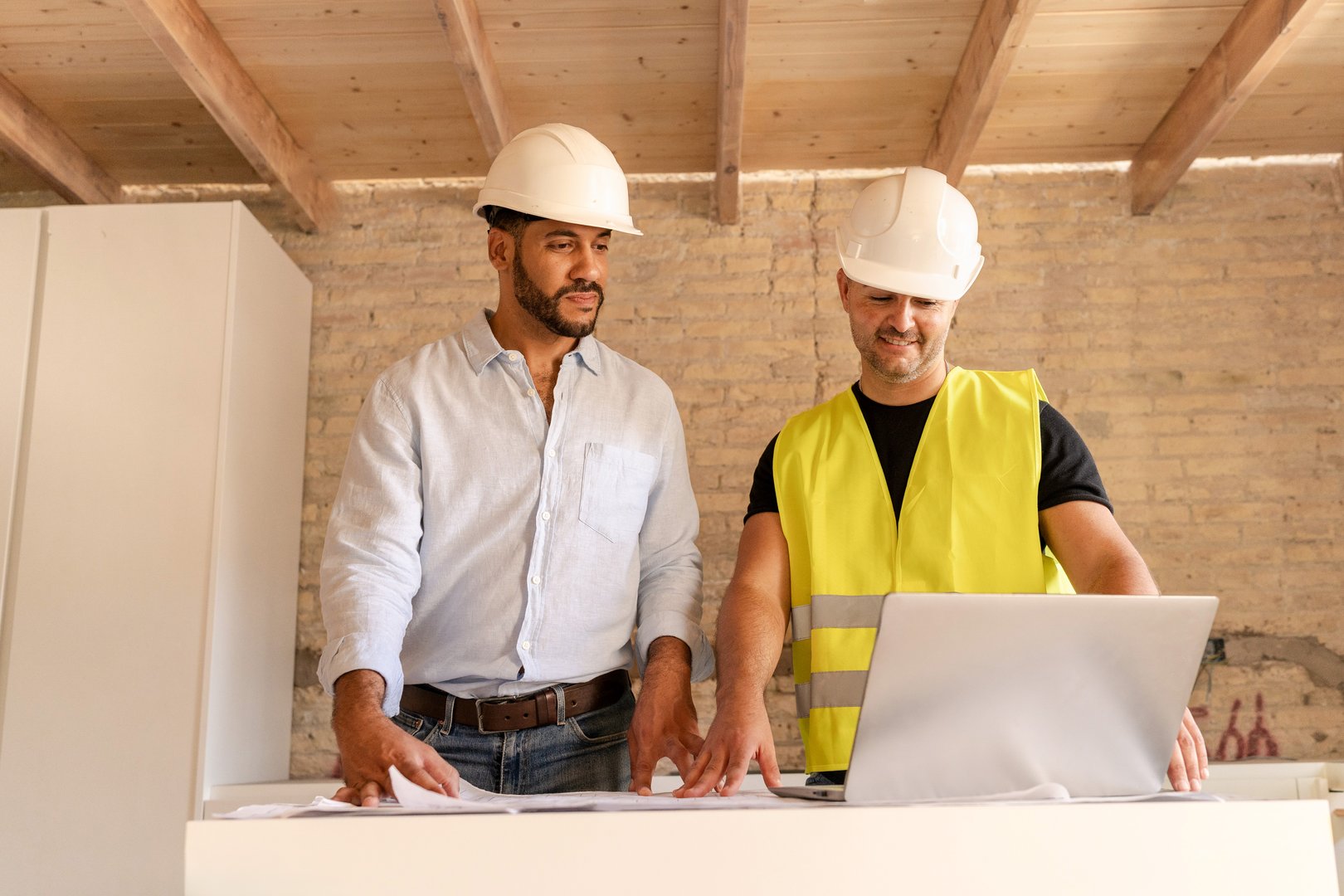 Construction workers discussing blueprint with customer using laptop in building under construction