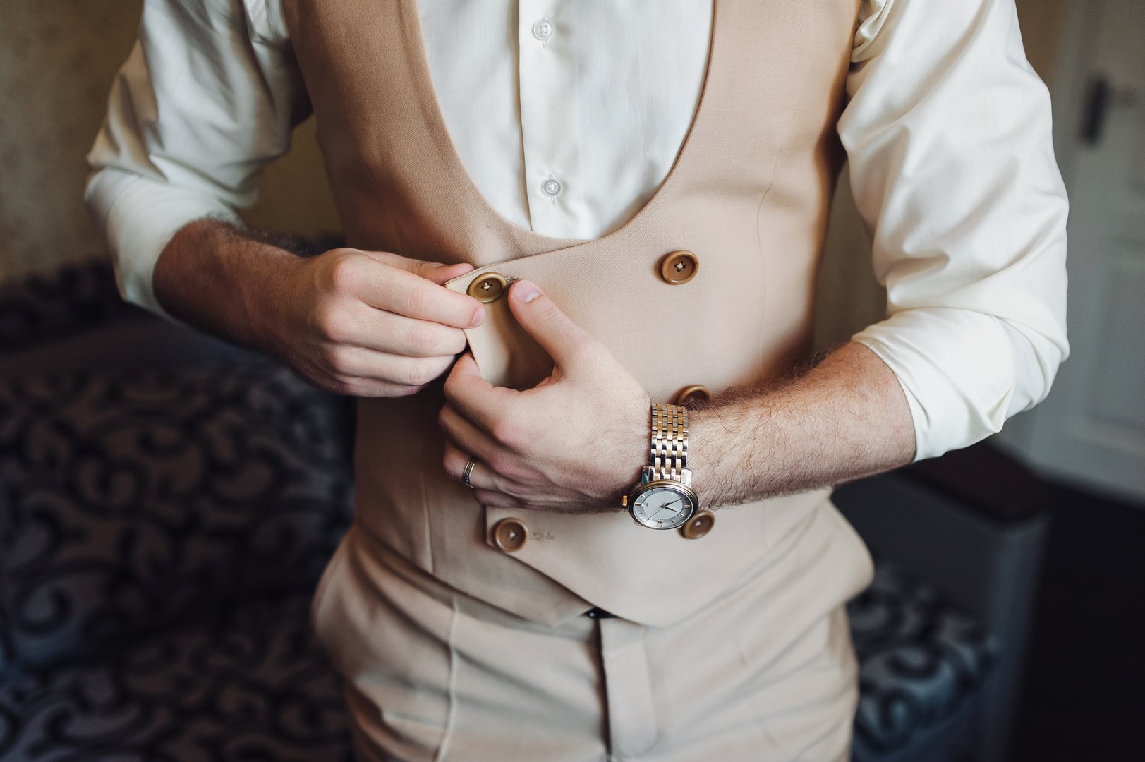 A man in a three-piece suit fastens buttons. Elegant groom. Wedding preparations.