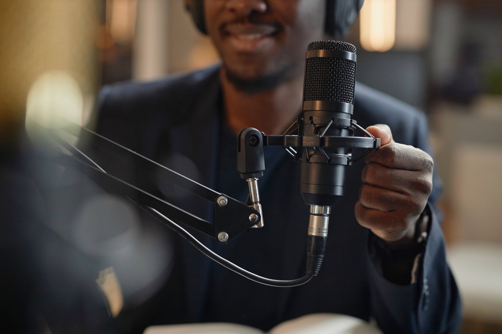 Close up shot of professional condenser microphone and African American male hand setting it up during live podcast in studio
