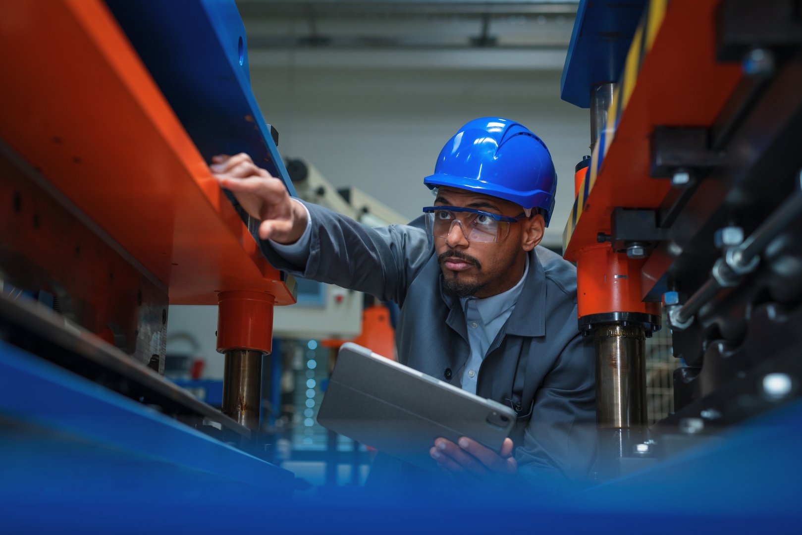 Engineer, with a blue helmet and safety glasses, checking manufacturing machinery, regulating the automatization process on a tablet, close up shot.