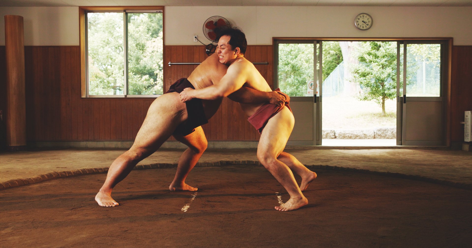 Athletes in motion, competitive young men, wrestlers in motion, competing, training against blue background in neon light. Concept of combat sport, martial arts, competition, tournament, athleticism