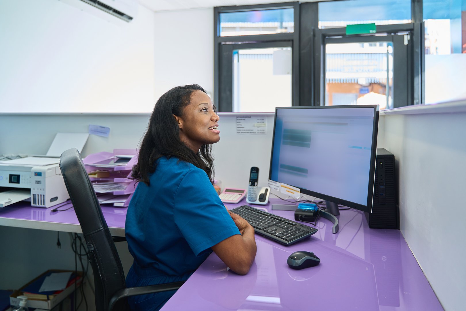 Smiling black female receptionist working at her desk in a modern dental clinic, using computer software to manage patient data and appointments