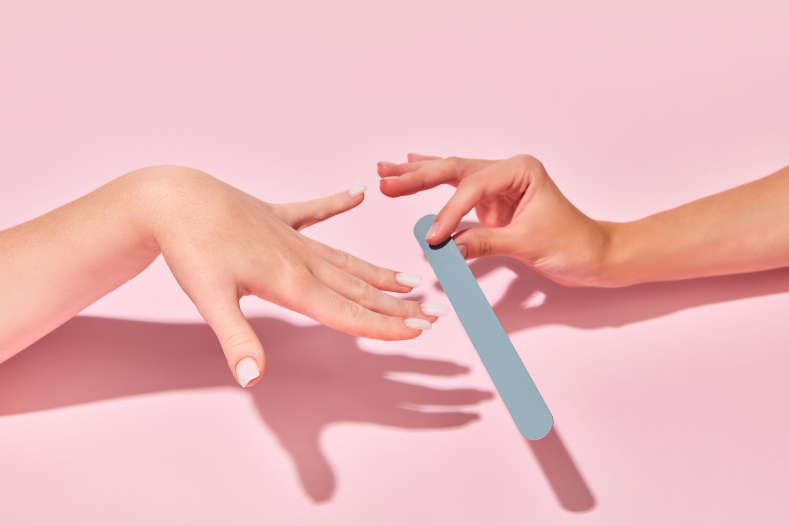 Female hand with nail file taking care after hands, nails against pink background. Elegant natural look. Concept of hand care, cosmetics and cosmetology, spa, natural beauty. Poster, ad